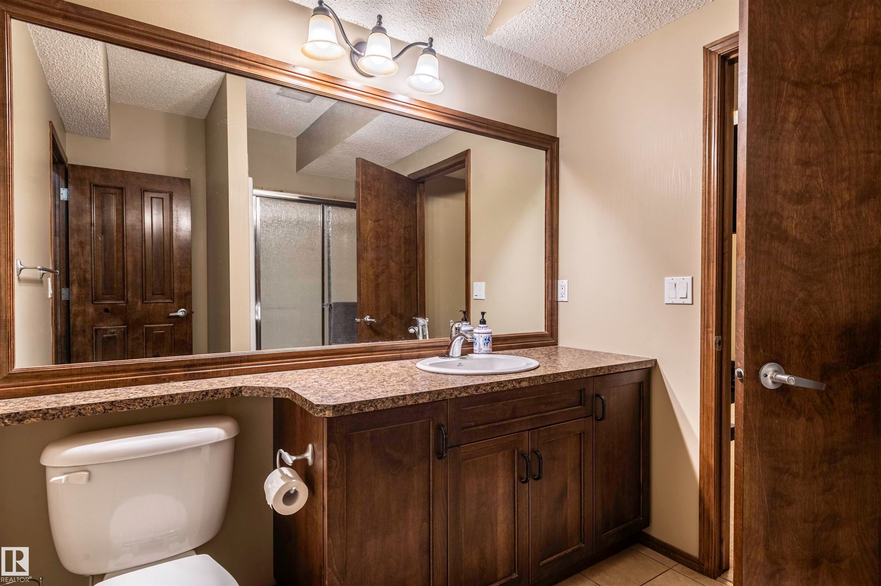 Bathroom featuring a vanity with a drop-in sink, granite-style countertop, dark wood-finish cabinetry, and an expansive framed mirror - 19 Newton Place, St. Albert, AB - Indoor Photo Showing Bathroom