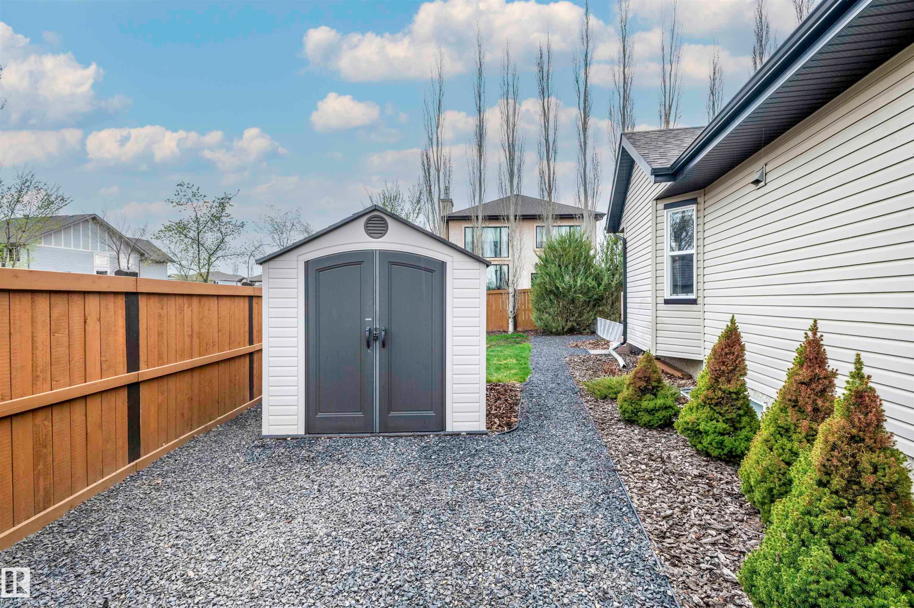 Gravel pathway featuring a freestanding shed with double doors, wood fencing, exterior siding, and foundation plantings - 19 Newton Place, St. Albert, AB - Outdoor