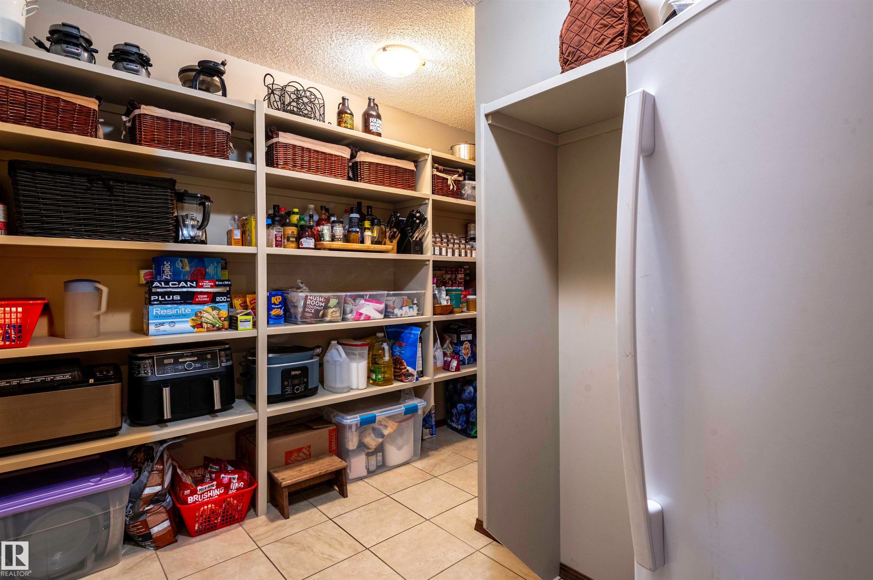Expansive pantry featuring extensive built-in shelving, tiled flooring, and an overhead light fixture - 19 Newton Place, St. Albert, AB - Indoor
