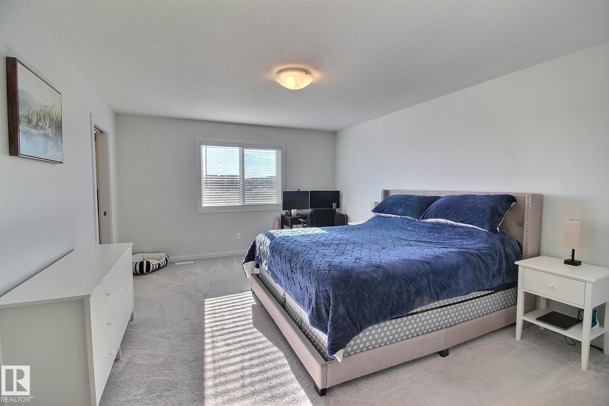 Spacious room featuring light-colored carpeting, white wall finishes, a large window with blinds, and an overhead flush-mount light fixture - 121 Stiles Bend, Leduc, AB - Indoor Photo Showing Bedroom