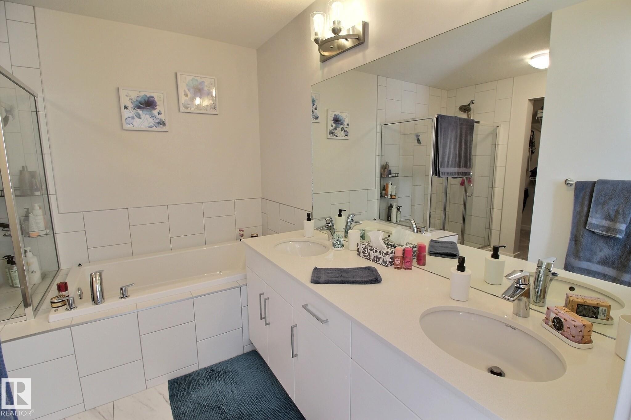 Bathroom featuring a built-in tub with tile surround, a spacious vanity with dual sinks, a large wall-mounted mirror, and a separate glass-enclosed shower - 121 Stiles Bend, Leduc, AB - Indoor Photo Showing Bathroom