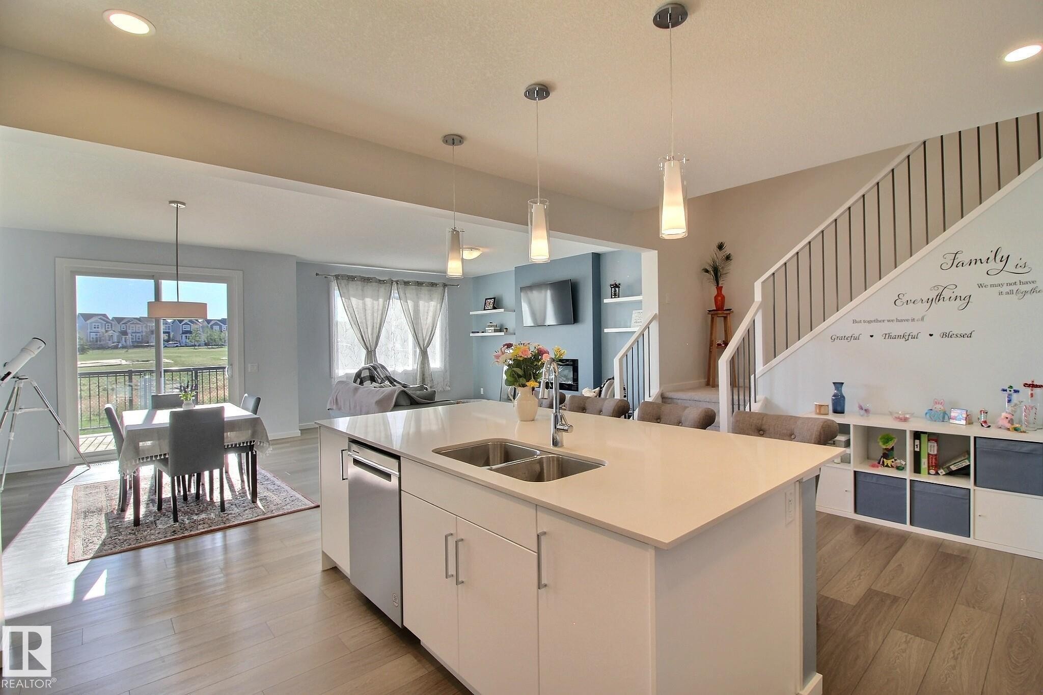 Open-concept kitchen featuring a large island with an undermount double sink, stainless steel appliances, pendant lighting, and wood-finish flooring - 121 Stiles Bend, Leduc, AB - Indoor Photo Showing Kitchen With Double Sink With Upgraded Kitchen