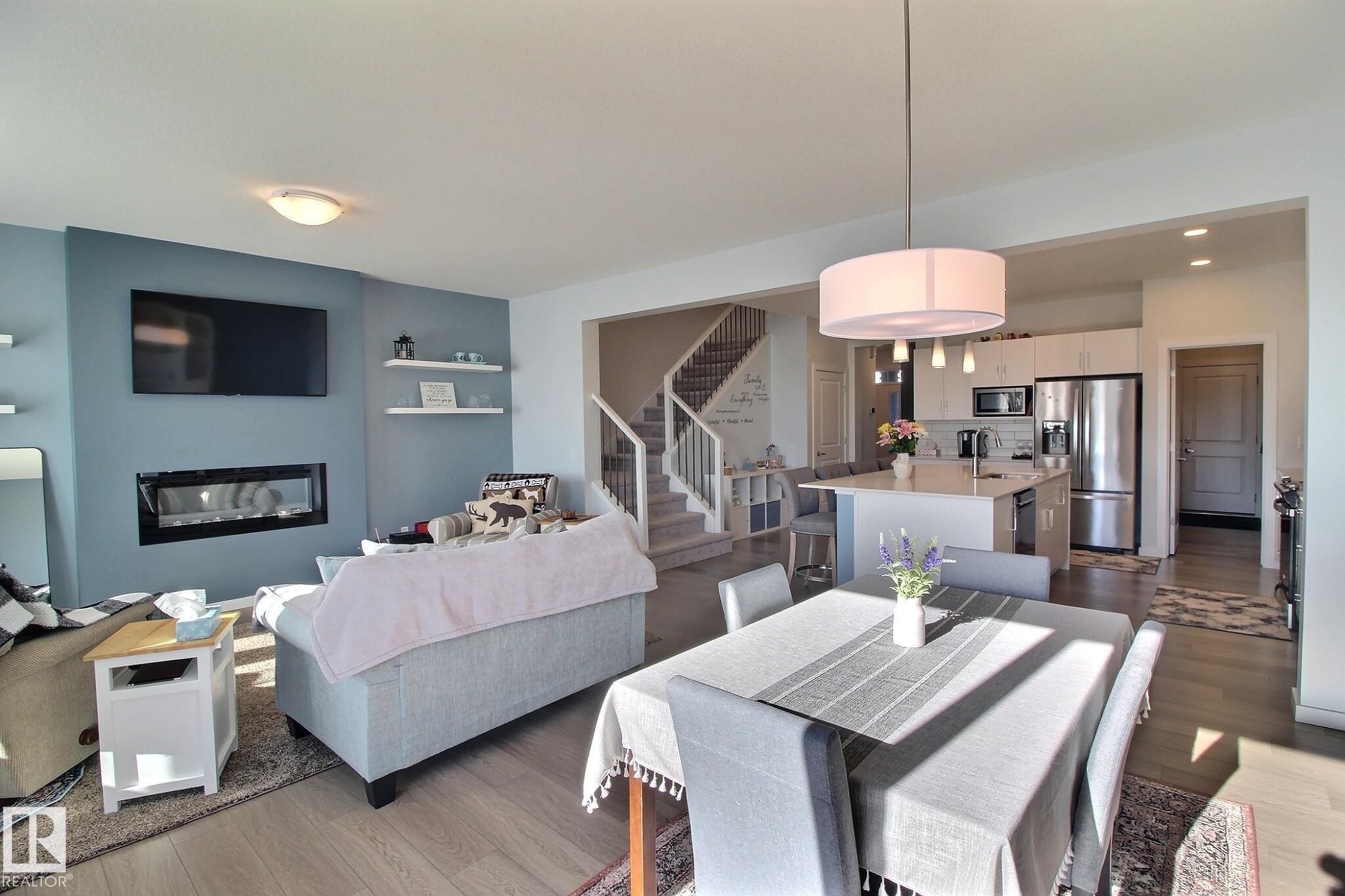 Open-concept living space featuring wood-finish flooring, a contemporary fireplace, and a kitchen with stainless steel appliances - 121 Stiles Bend, Leduc, AB - Indoor With Fireplace