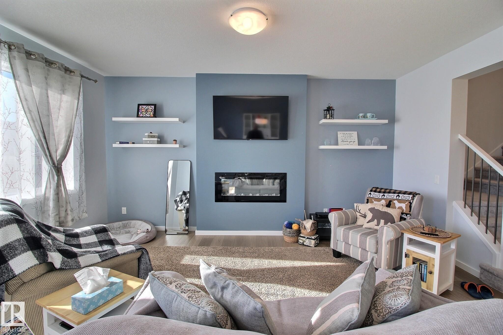Living area featuring a floor-to-ceiling accent wall, built-in fireplace, and overhead lighting - 121 Stiles Bend, Leduc, AB - Indoor Photo Showing Living Room With Fireplace