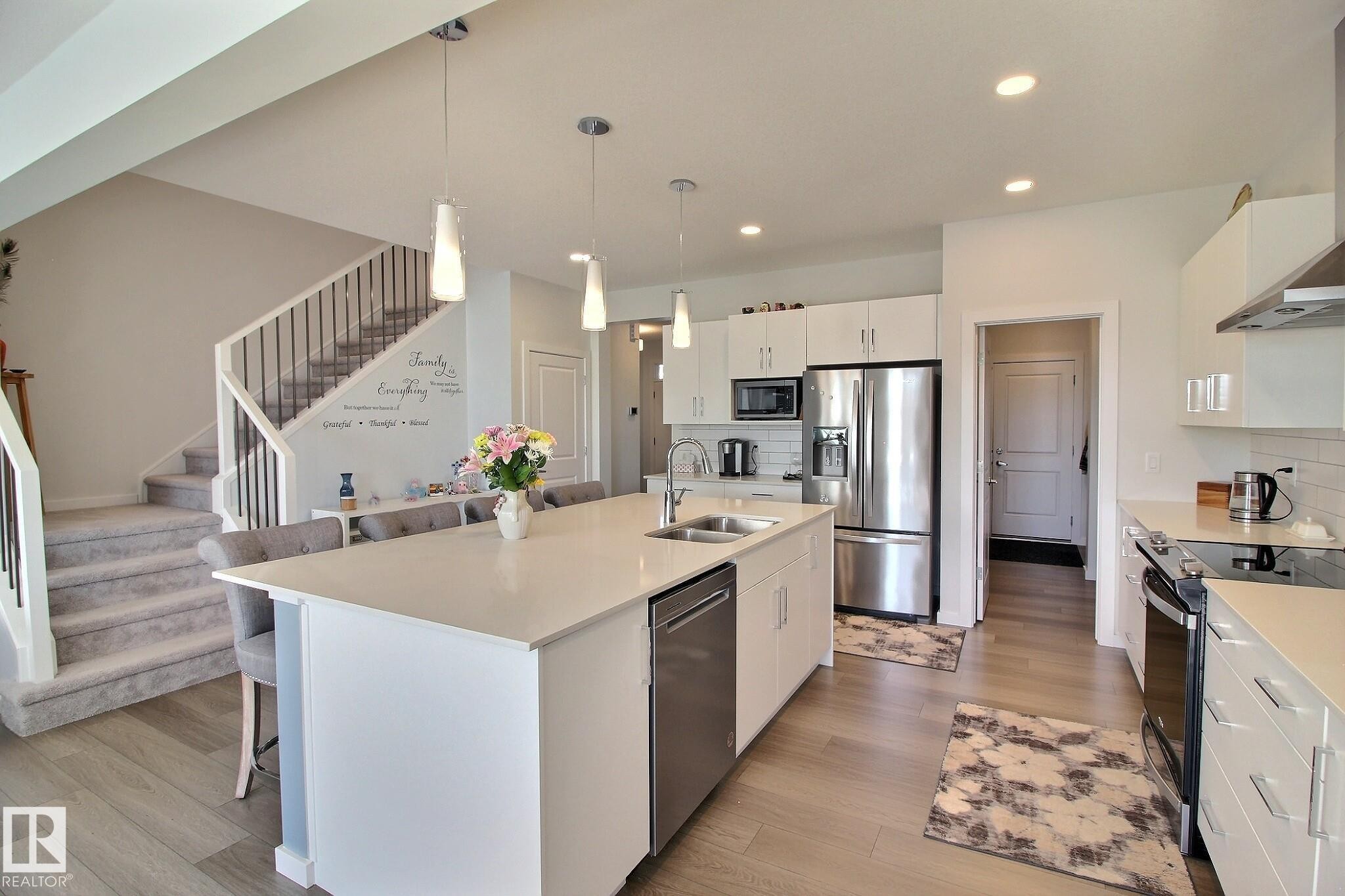 Modern kitchen featuring a large central island with seating, white shaker cabinetry, stainless steel appliances, and light wood-finish flooring - 121 Stiles Bend, Leduc, AB - Indoor Photo Showing Kitchen With Double Sink With Upgraded Kitchen