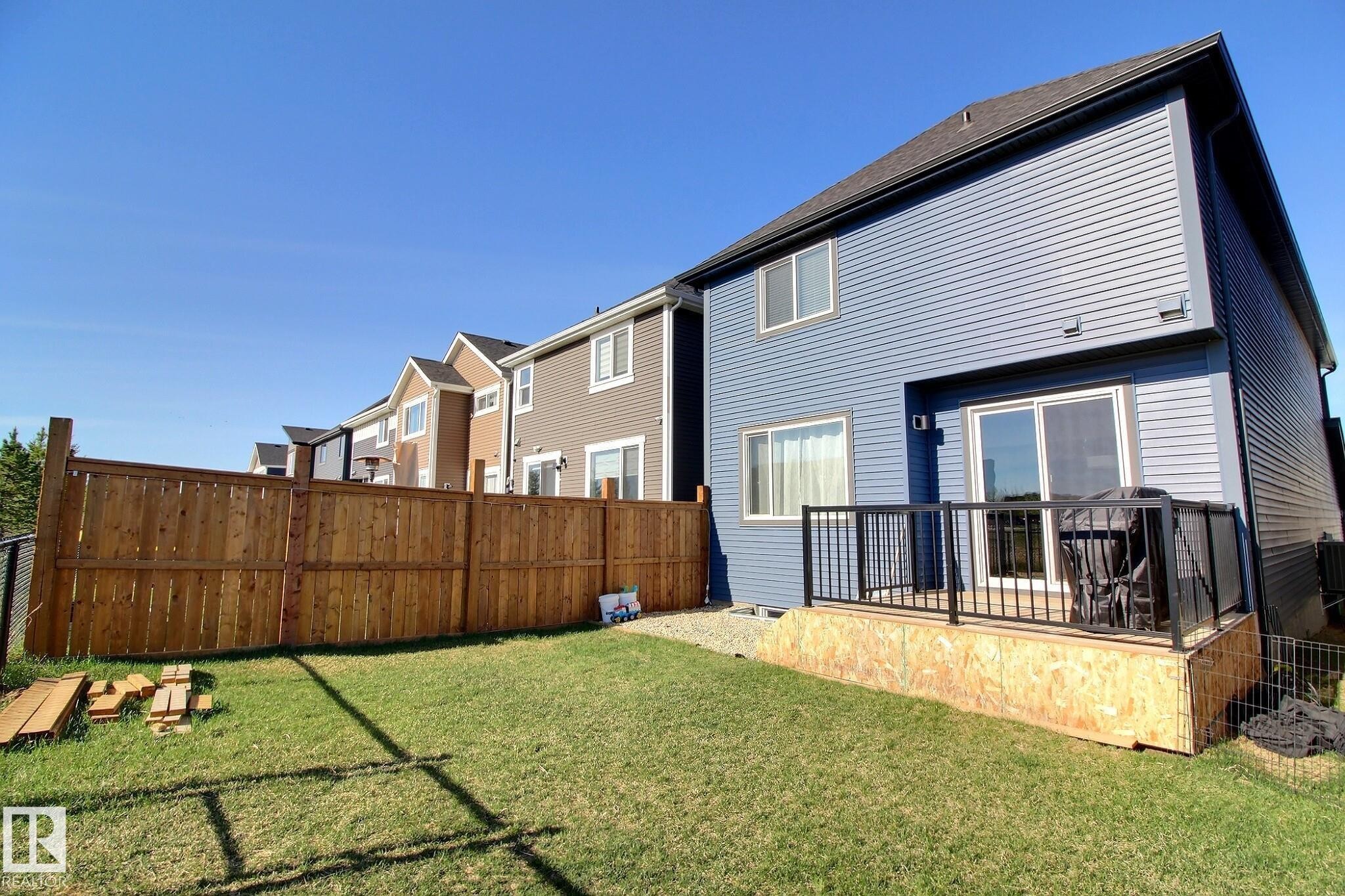 Private backyard featuring a wooden fence, a manicured lawn, and a raised wooden deck with black metal railings - 121 Stiles Bend, Leduc, AB - Outdoor