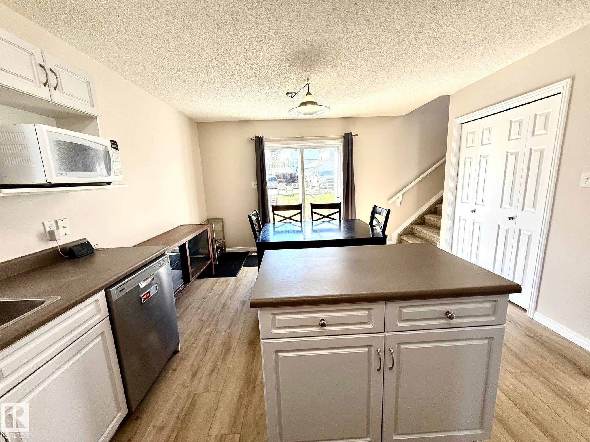 Kitchen featuring a center island with storage, white cabinetry, integrated stainless steel dishwasher, and wood-finish flooring - 645 Windross Crescent, Edmonton, AB