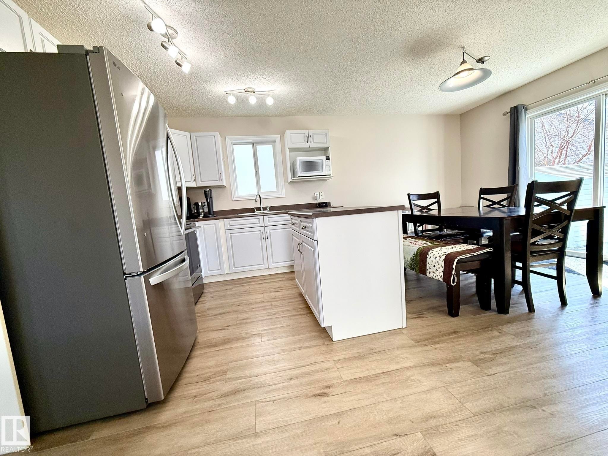 Kitchen featuring white cabinetry, stainless steel refrigerator, dark countertops, and wood-finish flooring - 645 Windross Crescent, Edmonton, AB