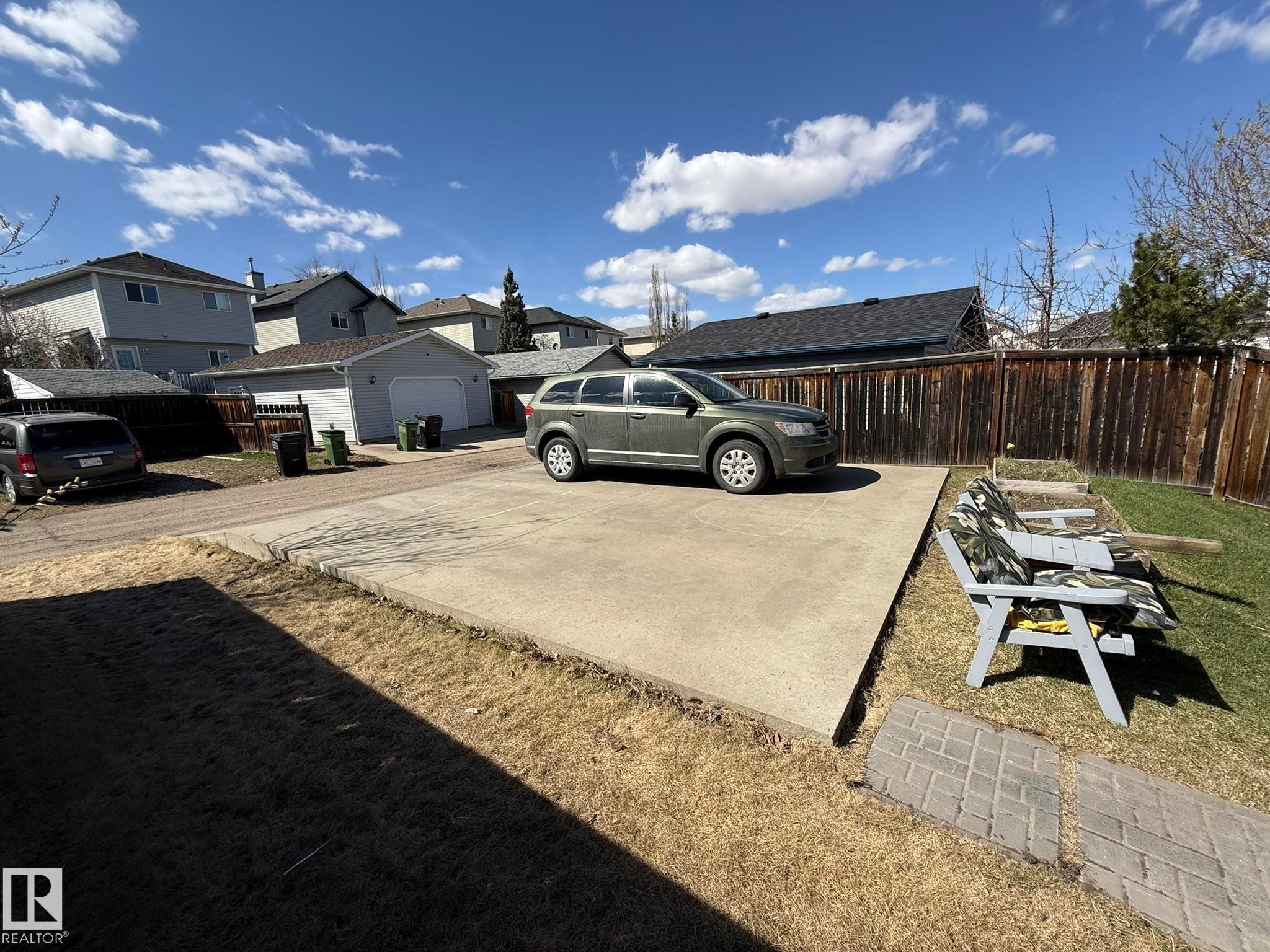 Rear yard with concrete parking pad, wood plank fencing, and a paver stone pathway - 645 Windross Crescent, Edmonton, AB
