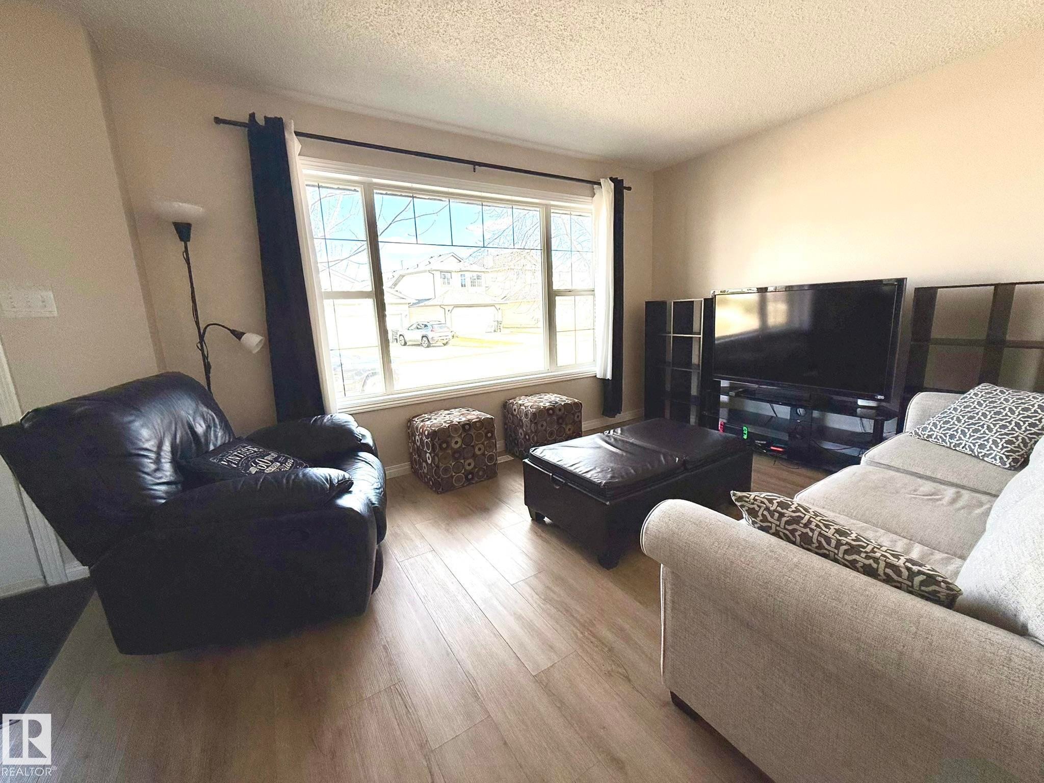 Living area featuring wood-finish flooring, a large window with white trim, and neutral wall tones - 645 Windross Crescent, Edmonton, AB