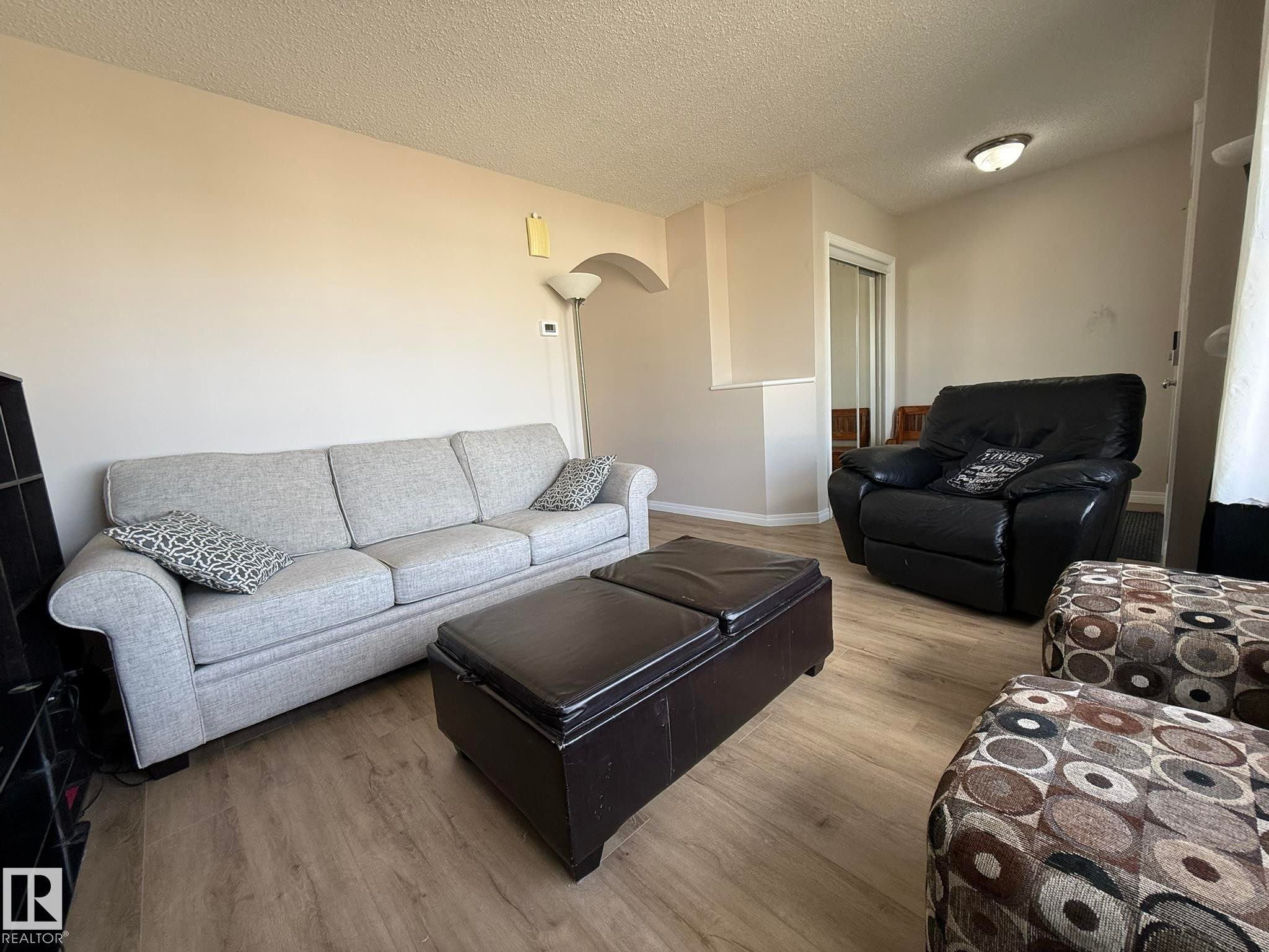 Bright living area featuring wood-finish flooring, neutral-toned walls, and a textured ceiling - 645 Windross Crescent, Edmonton, AB
