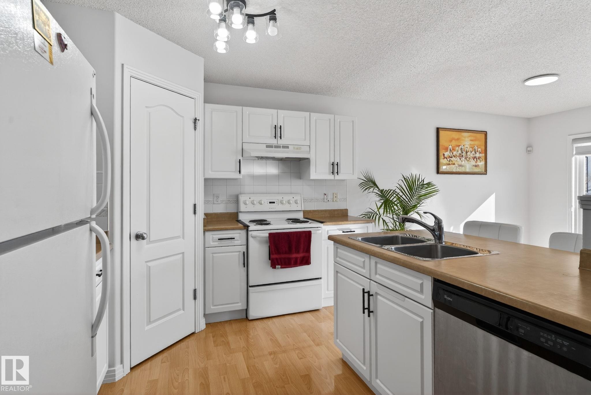Kitchen featuring white cabinetry, light wood-finish flooring, and light-toned countertops - 421 84 Street, Edmonton, AB - Indoor Photo Showing Kitchen With Double Sink