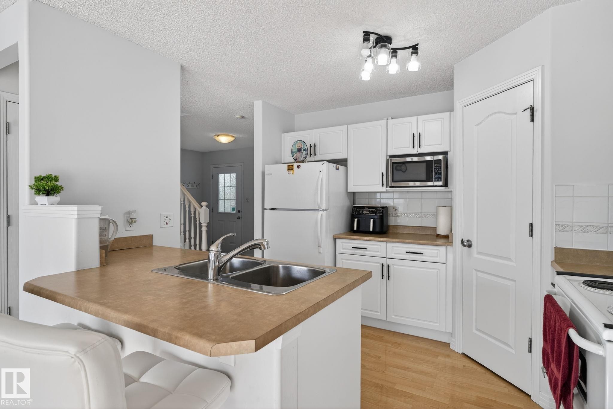 Kitchen featuring white cabinetry, a double basin stainless steel sink, a built-in microwave, light wood-finish flooring, and track lighting - 421 84 Street, Edmonton, AB - Indoor Photo Showing Kitchen With Double Sink