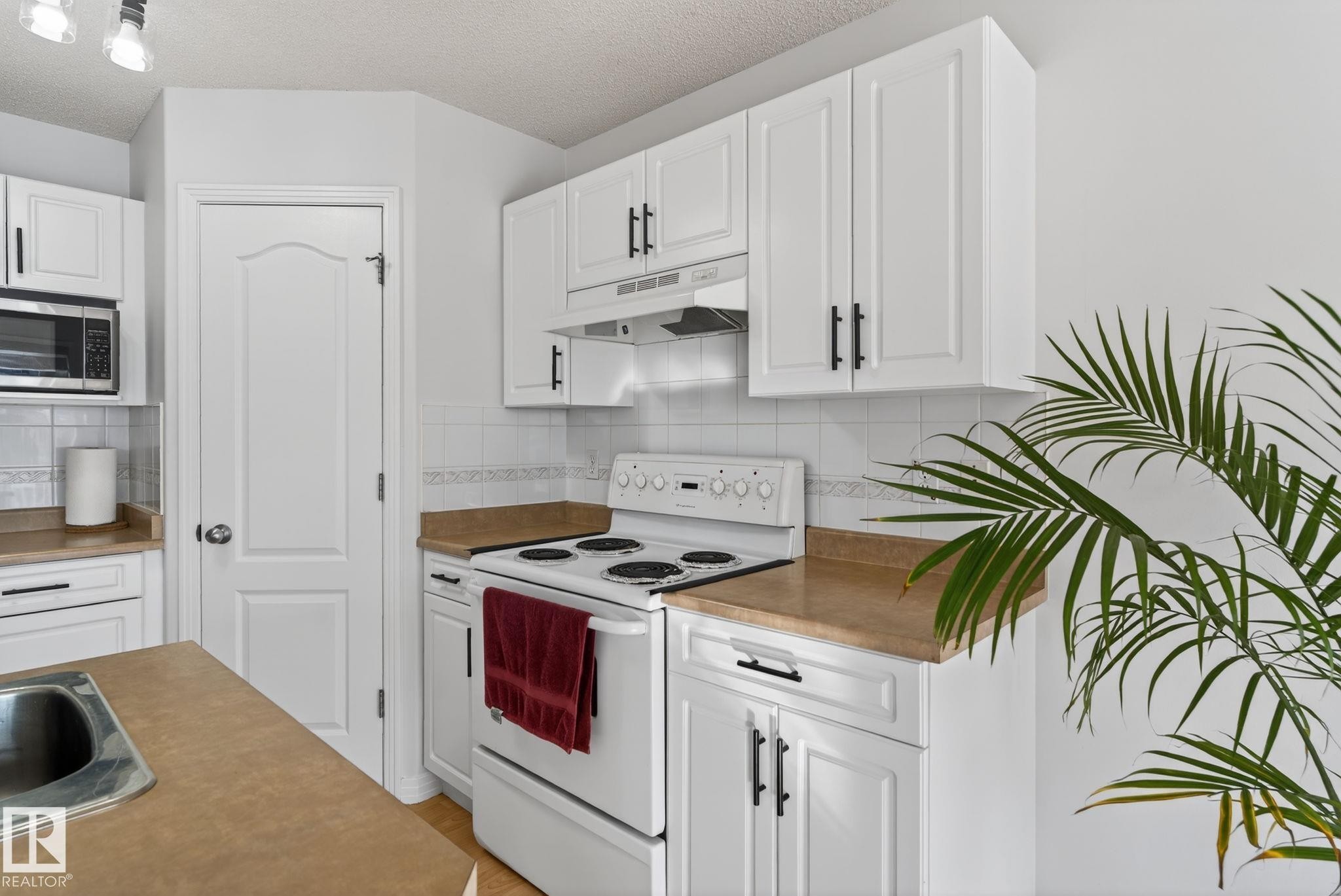 Kitchen featuring white cabinetry with black hardware, a white electric range with hood vent, and light brown countertops - 421 84 Street, Edmonton, AB - Indoor Photo Showing Kitchen