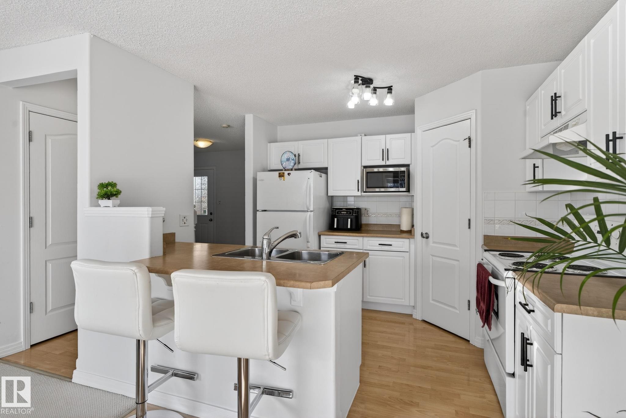 Kitchen with light wood-finish flooring, white cabinetry with black hardware, and light wood-tone countertops - 421 84 Street, Edmonton, AB - Indoor Photo Showing Kitchen With Double Sink