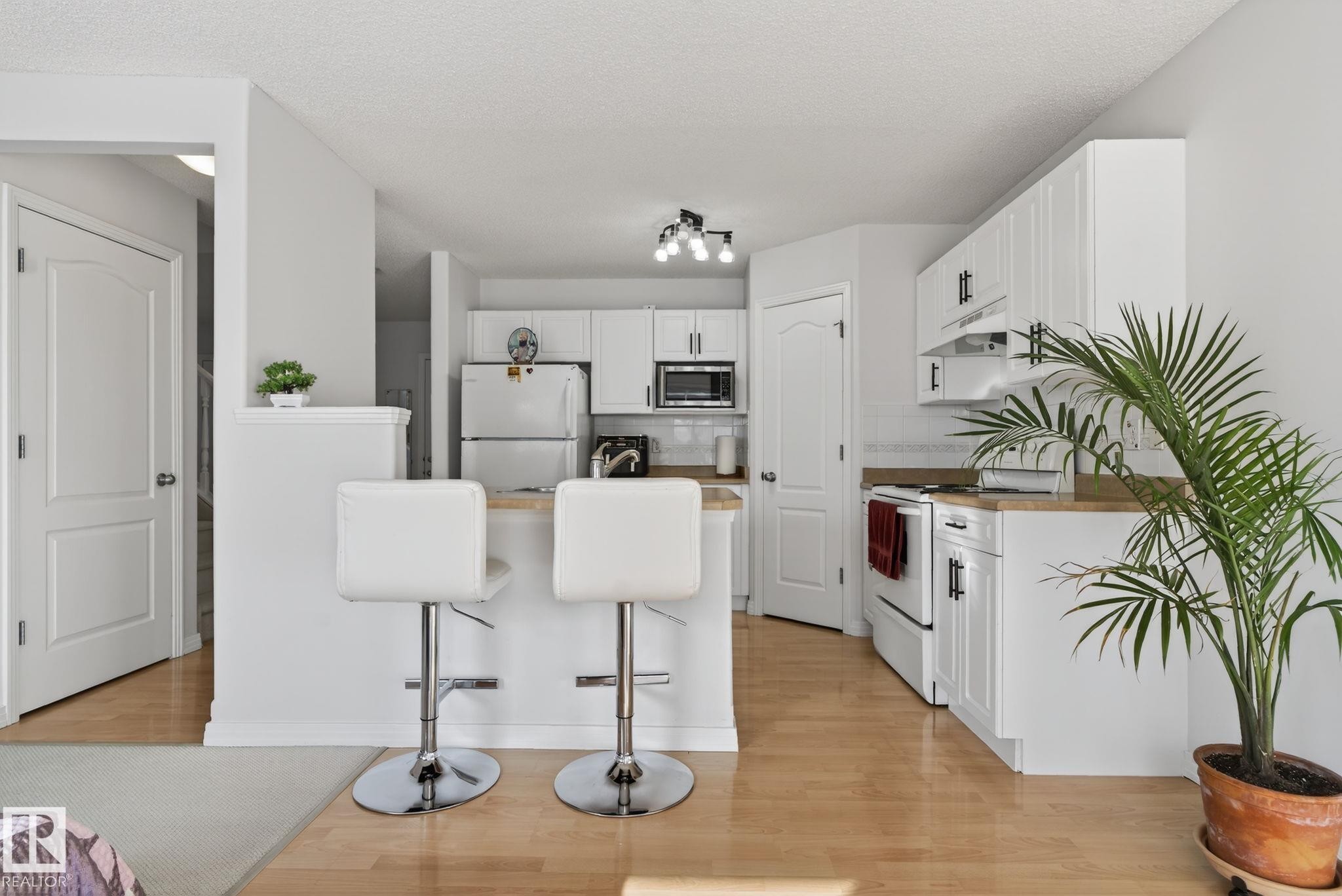 Galley kitchen featuring wood-finish flooring, white cabinetry with black hardware, light-toned countertops, and a white tile backsplash - 421 84 Street, Edmonton, AB - Indoor Photo Showing Kitchen