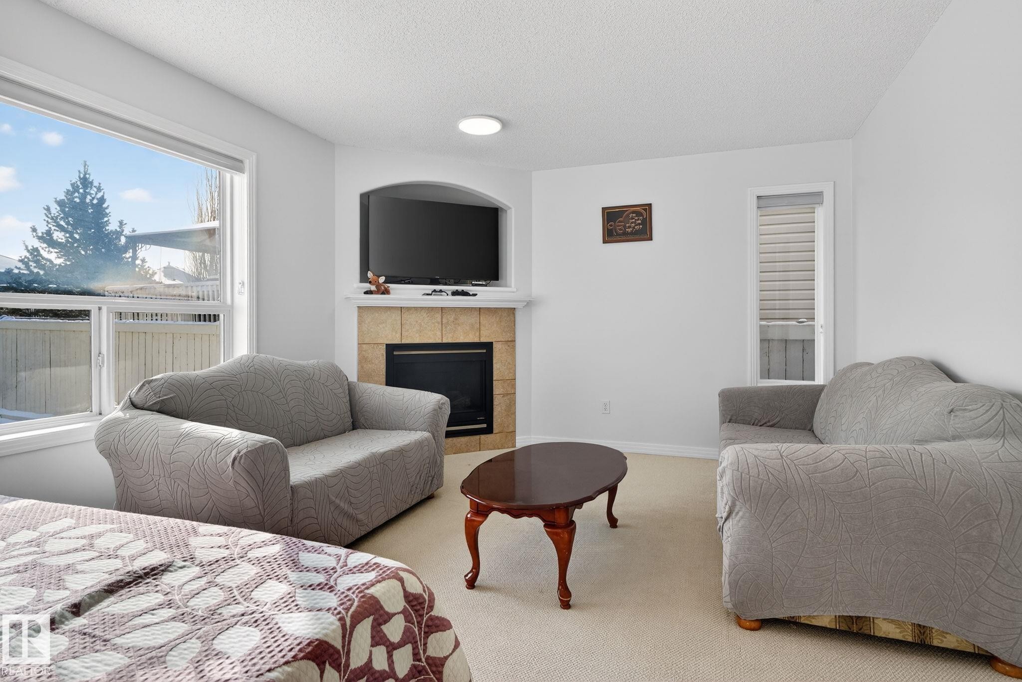 Living area featuring light-toned carpeting, a large window, and a built-in fireplace with a stone-finish surround - 421 84 Street, Edmonton, AB - Indoor Photo Showing Living Room With Fireplace
