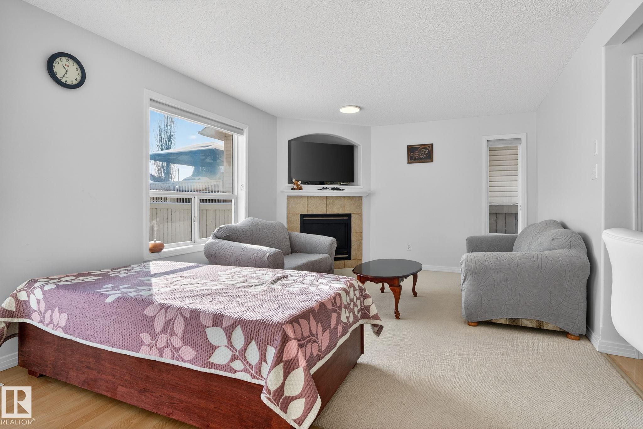 Living area featuring a corner fireplace with a tile surround and mantel, a large window, and light-toned carpeting - 421 84 Street, Edmonton, AB - Indoor Photo Showing Bedroom