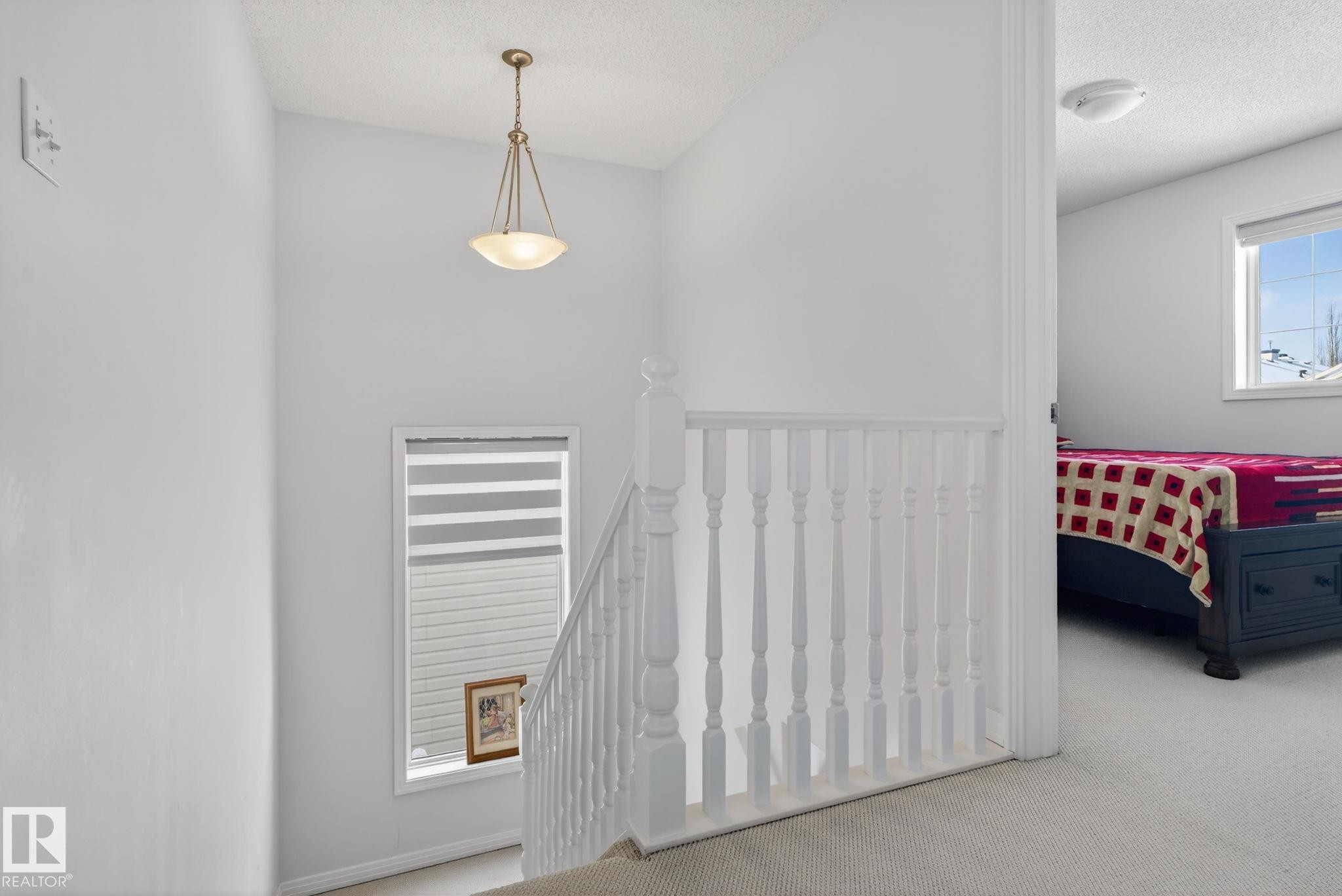 Carpeted staircase with white balusters and a pendant light fixture - 421 84 Street, Edmonton, AB - Indoor