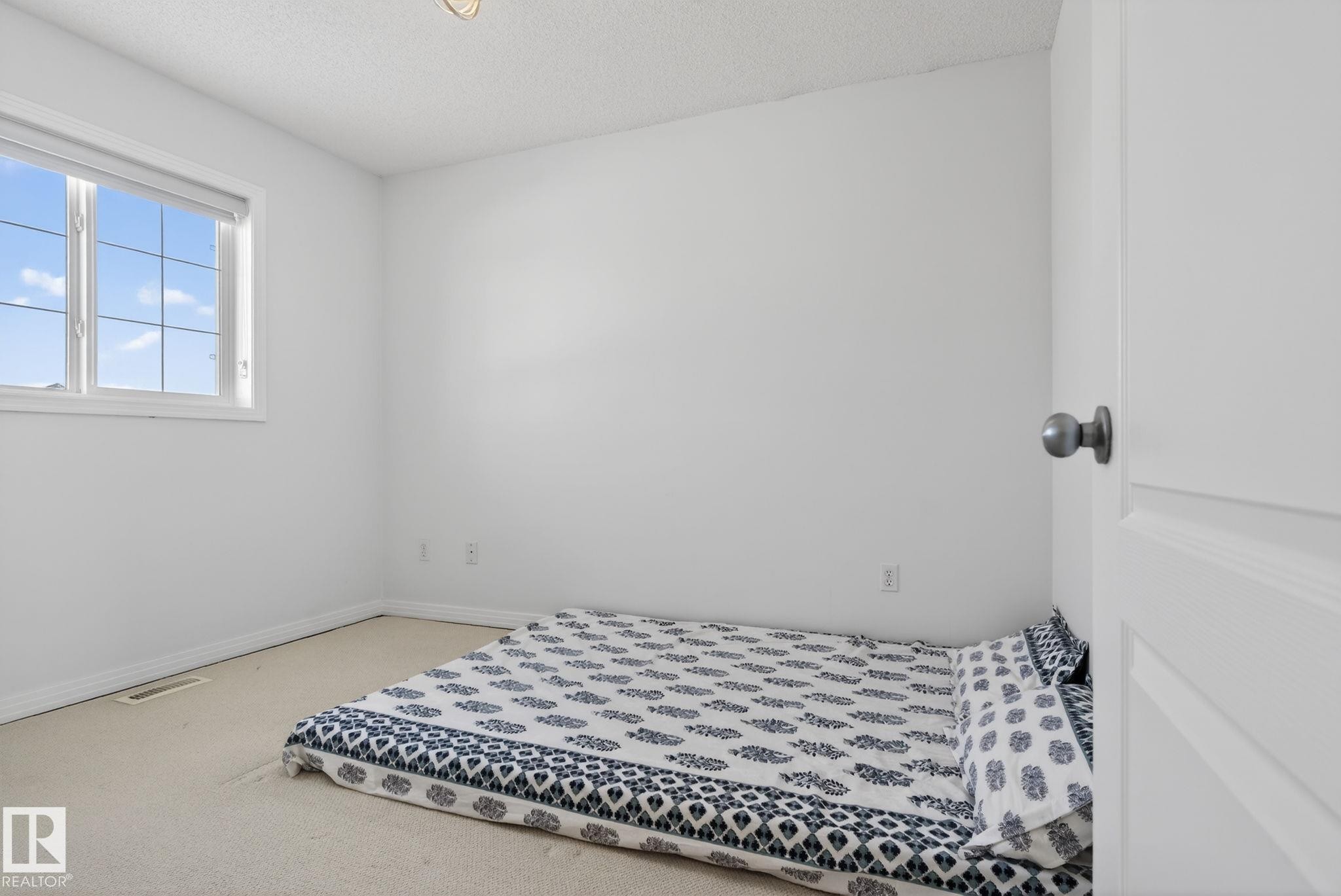 Bright room featuring a large window with white trim, neutral carpet, white walls, and a textured ceiling - 421 84 Street, Edmonton, AB - Indoor Photo Showing Bedroom