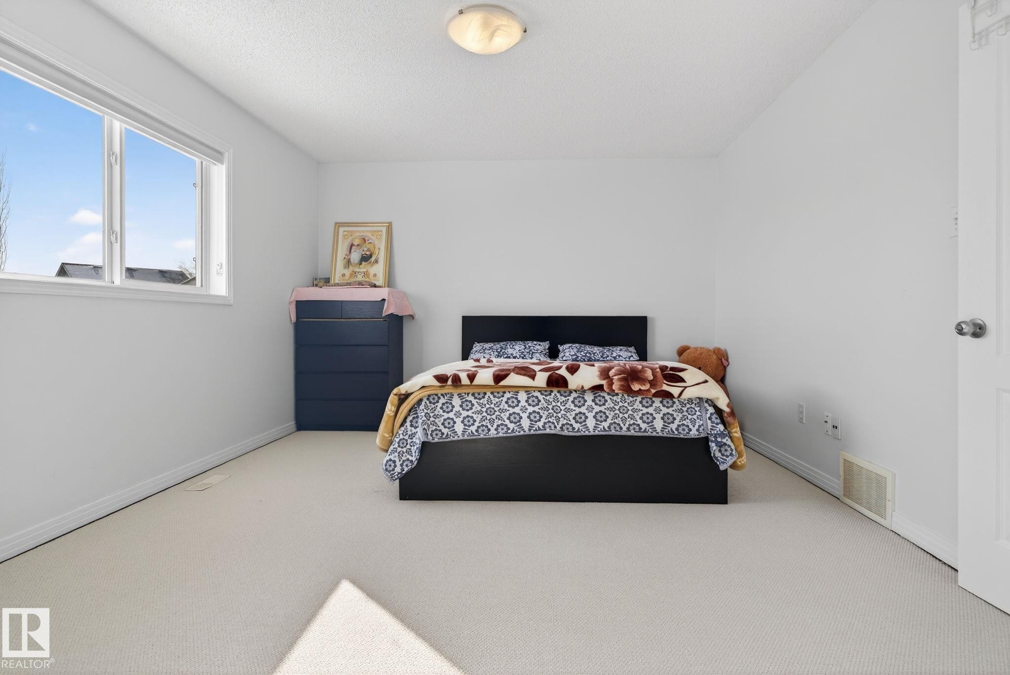 Carpeted room featuring white walls, a large window with white trim, and a white door with a silver knob - 421 84 Street, Edmonton, AB - Indoor Photo Showing Bedroom