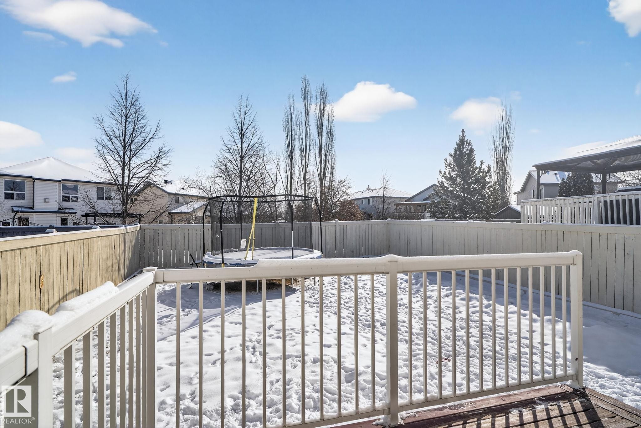 Spacious backyard featuring a wood deck with white railing, fenced perimeter, and mature trees - 421 84 Street, Edmonton, AB - Outdoor With Deck Patio Veranda