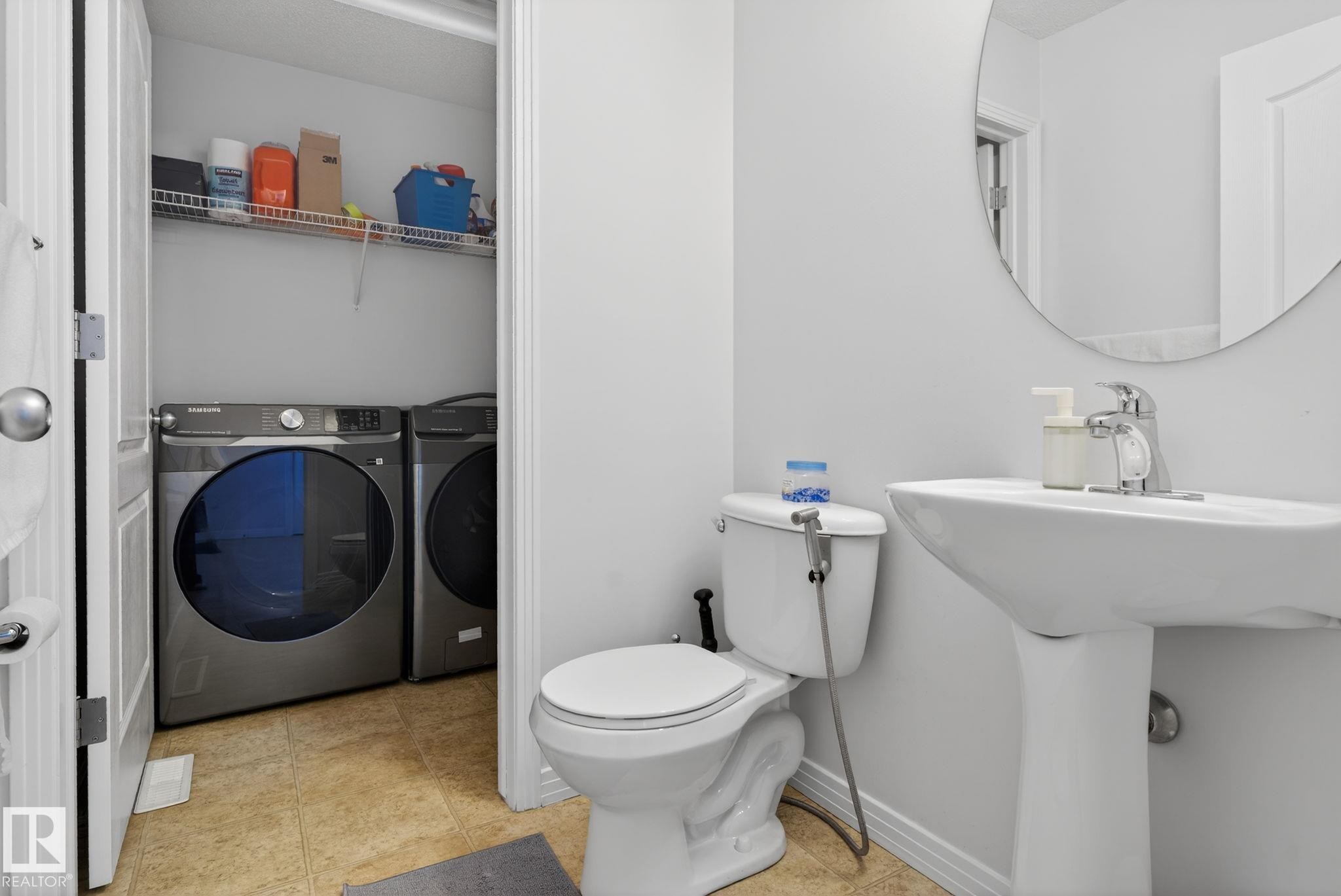 Compact laundry area featuring front-loading machines and an overhead wire shelf, accompanied by a pedestal sink and toilet - 421 84 Street, Edmonton, AB - Indoor Photo Showing Laundry Room