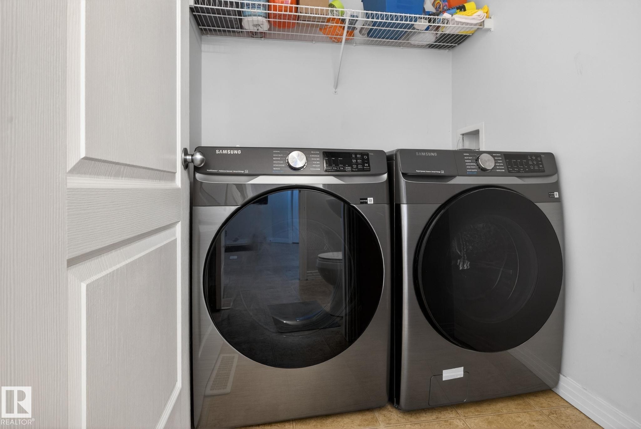 Dedicated laundry area featuring a front-loading washer and dryer set, wire shelving for storage, and durable floor tiling - 421 84 Street, Edmonton, AB - Indoor Photo Showing Laundry Room
