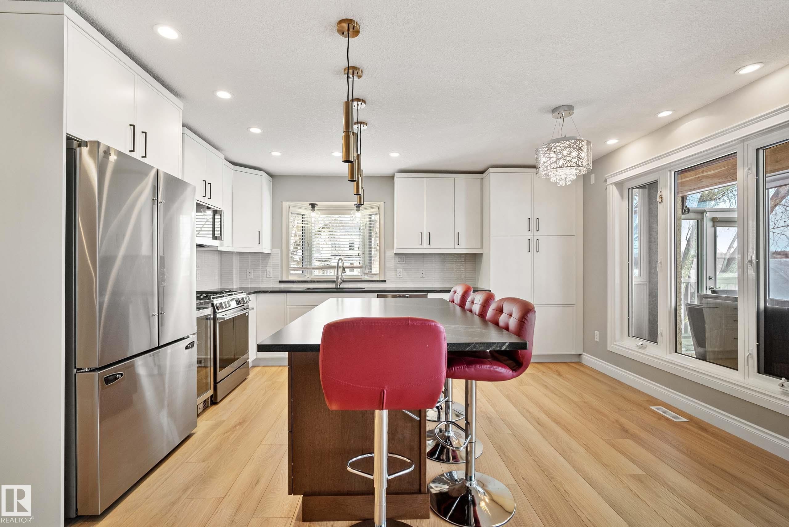Contemporary kitchen featuring wood-finish flooring, white cabinetry, dark countertops, a stainless steel refrigerator, and a kitchen island with seating - 104 Bayview Drive, Rural Parkland County, AB - Indoor Photo Showing Kitchen With Upgraded Kitchen