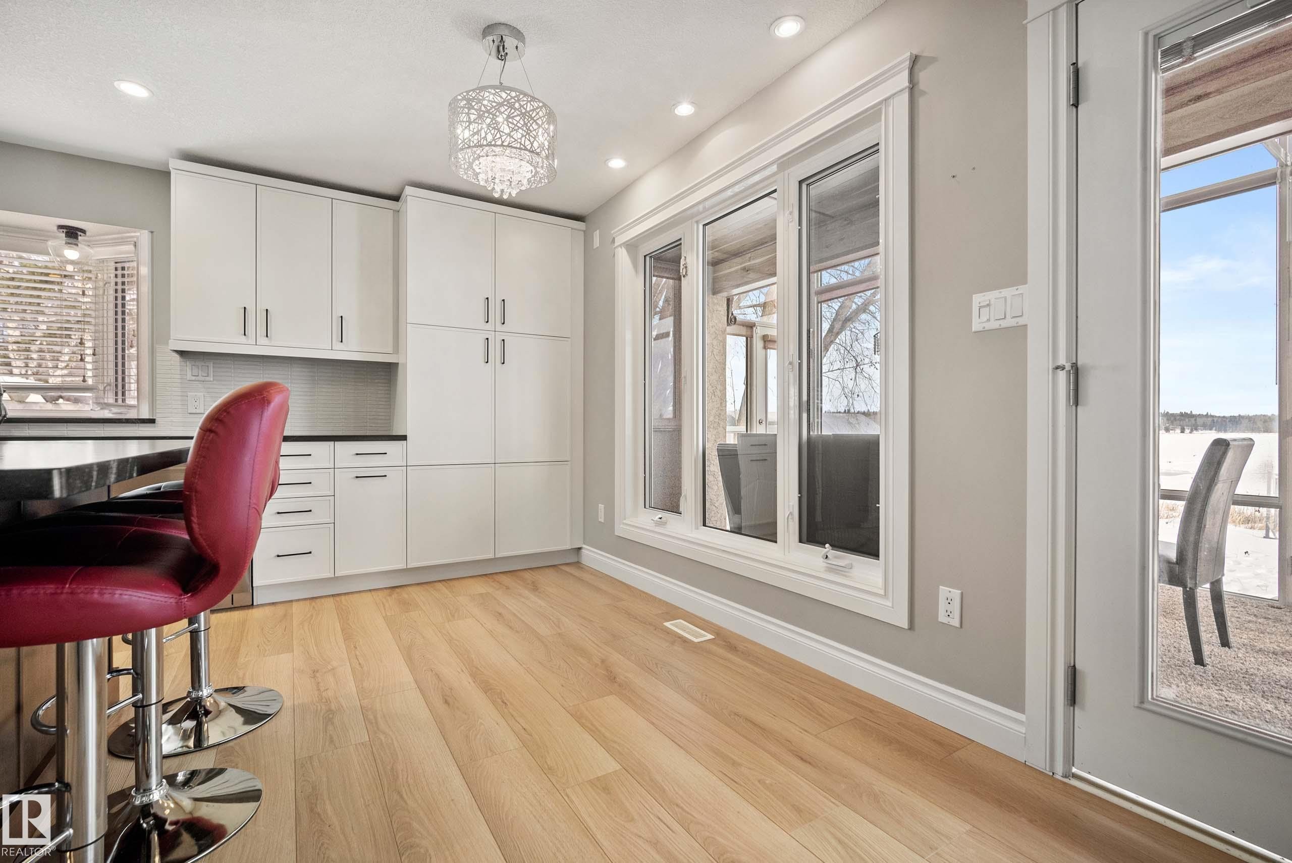 Kitchen area featuring light wood-finish flooring, white cabinetry, dark countertops, and a tile backsplash - 104 Bayview Drive, Rural Parkland County, AB - Indoor Photo Showing Other Room