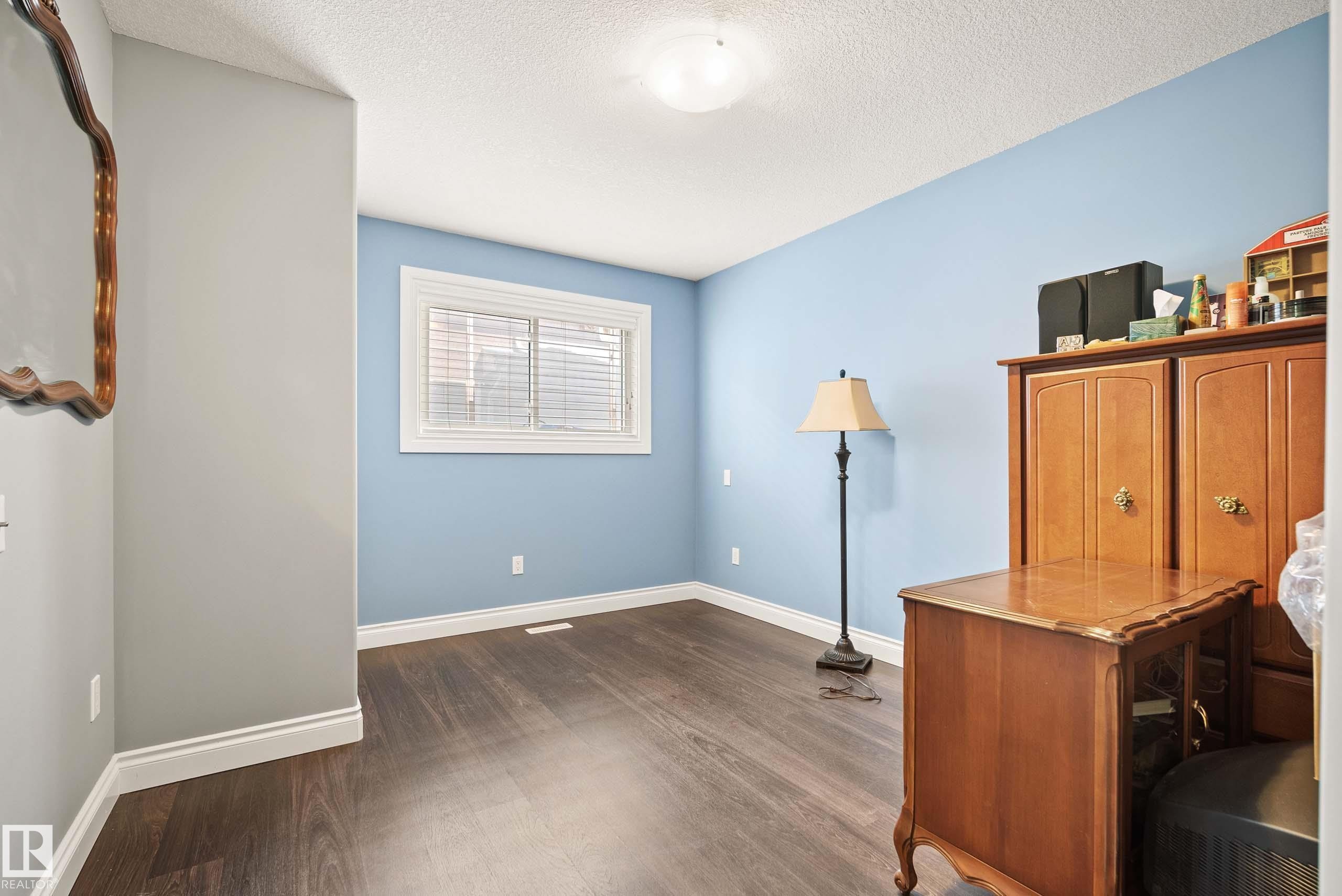 Room featuring wood-finish flooring, light blue and gray wall tones, a window with white trim and blinds, white baseboards, and a flush mount ceiling light fixture - 104 Bayview Drive, Rural Parkland County, AB - Indoor Photo Showing Other Room