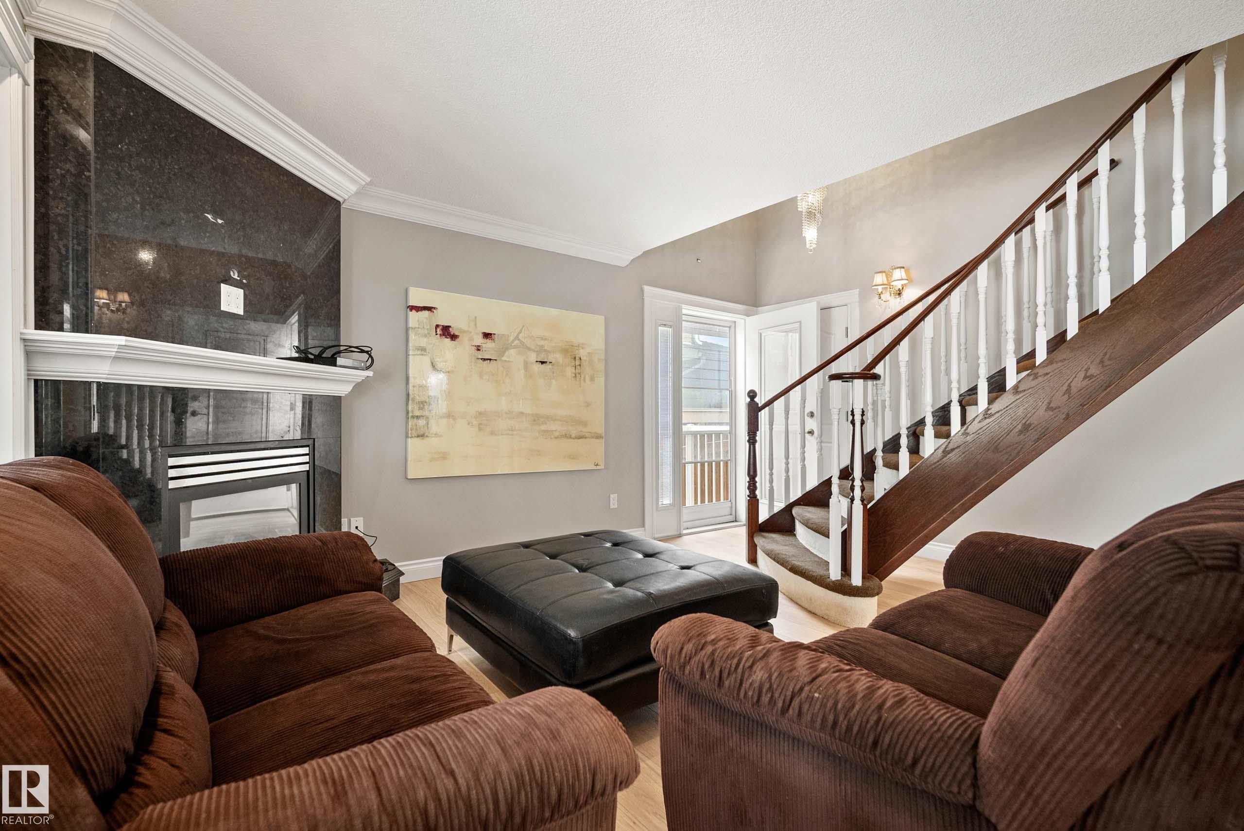 Living area featuring a dark stone-clad fireplace with a white mantel, wood-finish flooring, and a staircase with a dark wood handrail and white balusters - 104 Bayview Drive, Rural Parkland County, AB - Indoor