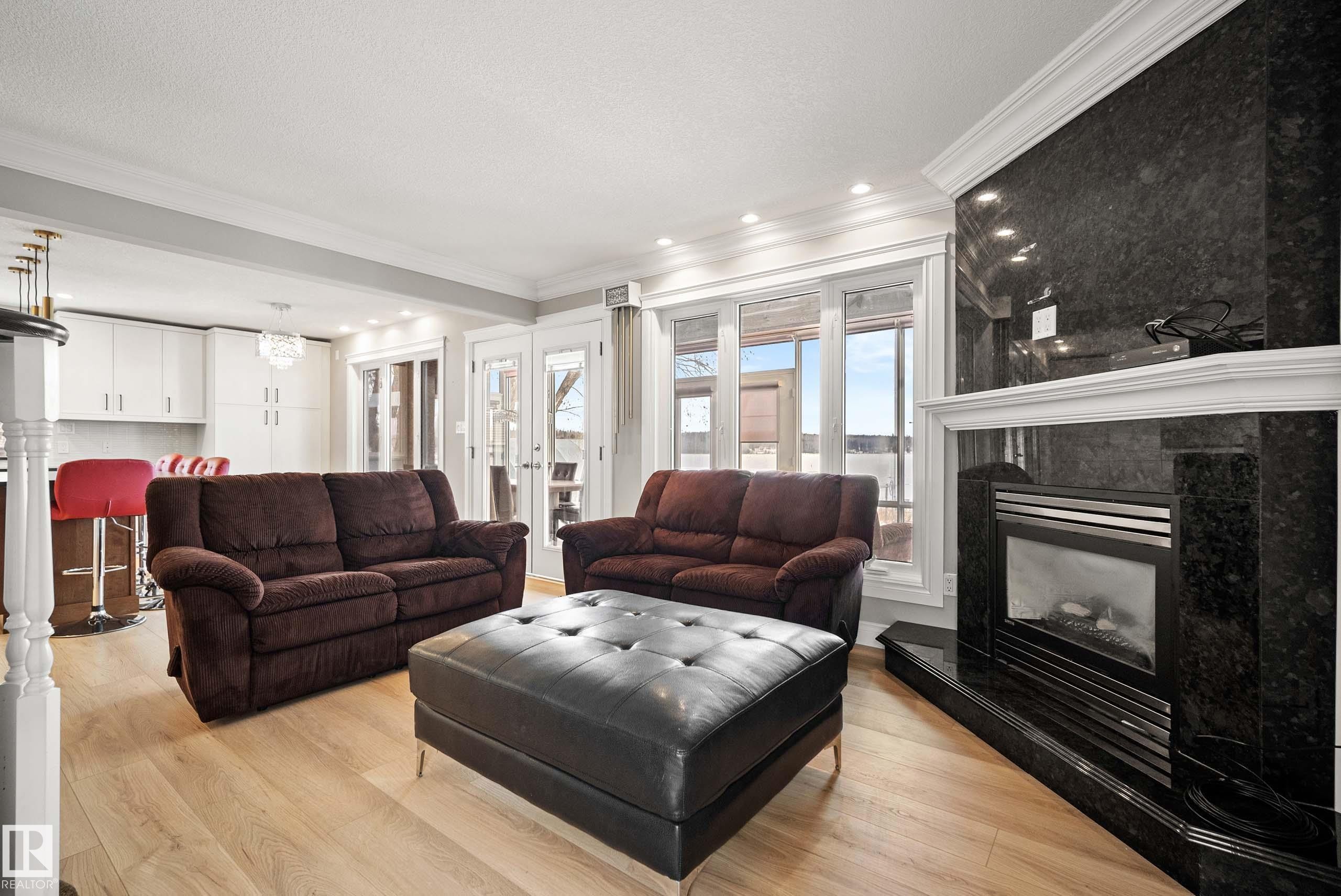 Living area featuring a black stone fireplace with a white mantel, light wood-finish flooring, and crown molding - 104 Bayview Drive, Rural Parkland County, AB - Indoor Photo Showing Living Room With Fireplace