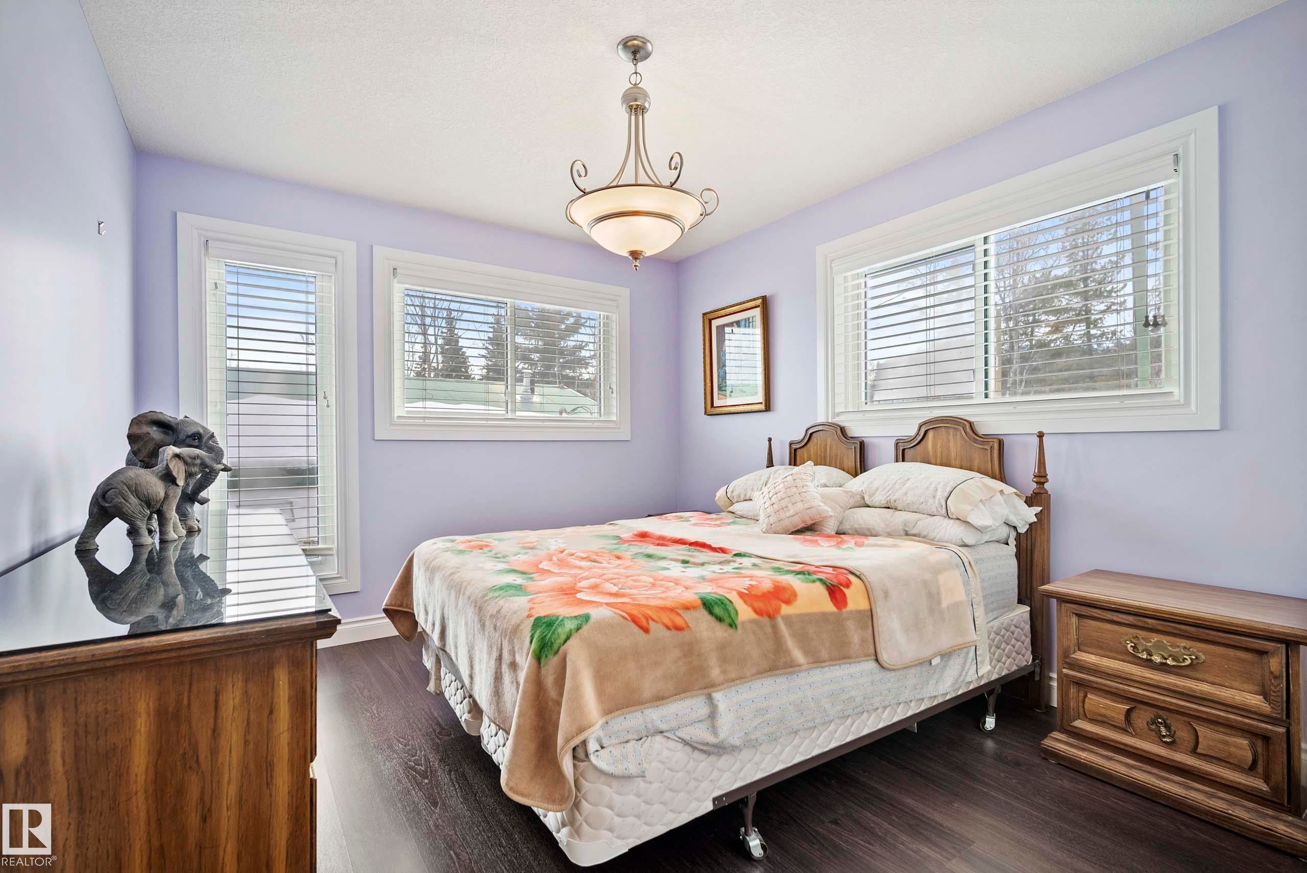 Spacious bedroom featuring dark wood-finish flooring, two large windows with white trim, and a ceiling-mounted light fixture - 104 Bayview Drive, Rural Parkland County, AB - Indoor Photo Showing Bedroom