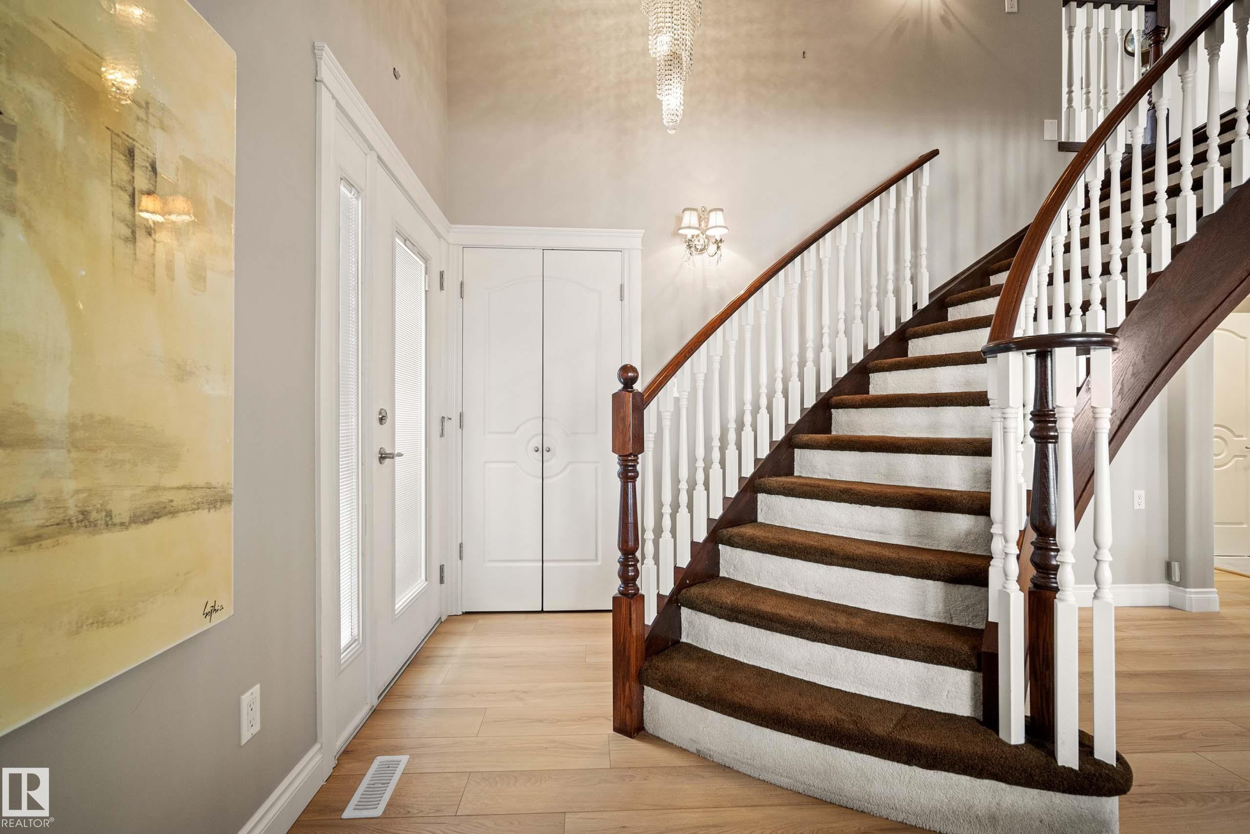Grand curved staircase with dark wood handrails, white balusters, and carpeted treads - 104 Bayview Drive, Rural Parkland County, AB - Indoor Photo Showing Other Room