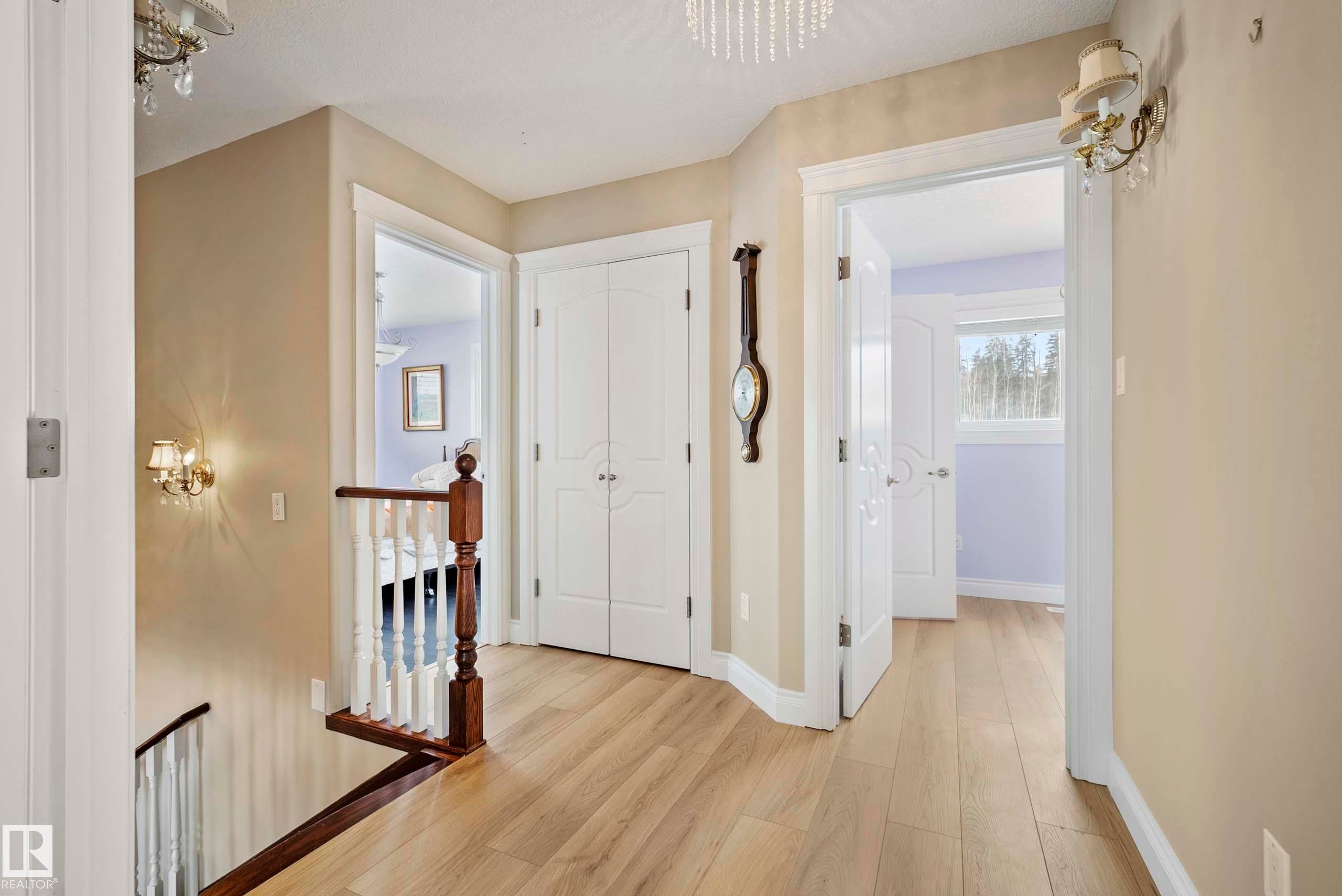 Upper landing featuring wood-finish flooring, white spindle railing with dark wood banister, and an ornate crystal chandelier - 104 Bayview Drive, Rural Parkland County, AB - Indoor Photo Showing Other Room