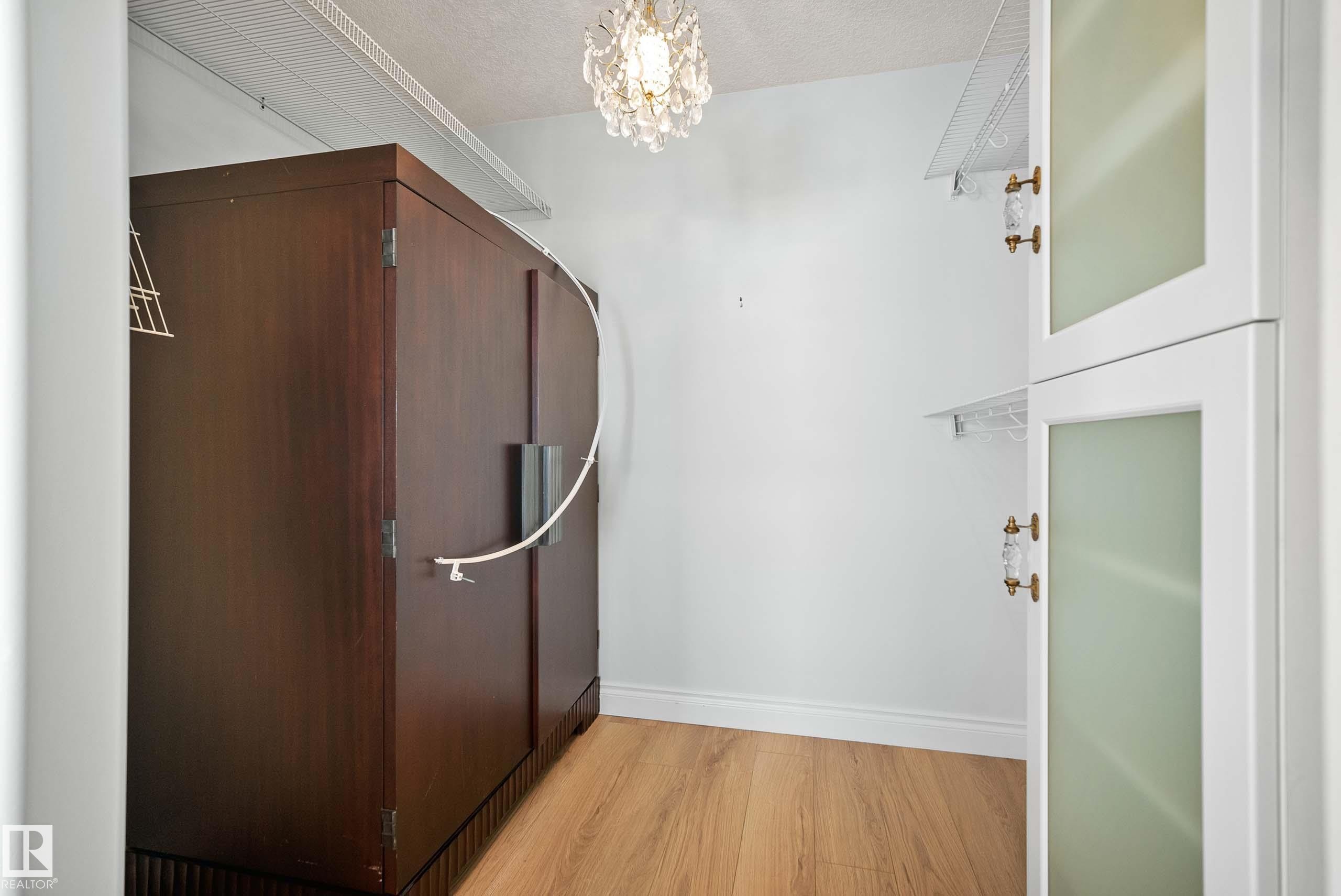 Custom closet featuring a large dark wood-finish armoire, wood-finish flooring, white wire shelving, and a decorative chandelier - 104 Bayview Drive, Rural Parkland County, AB - Indoor Photo Showing Other Room