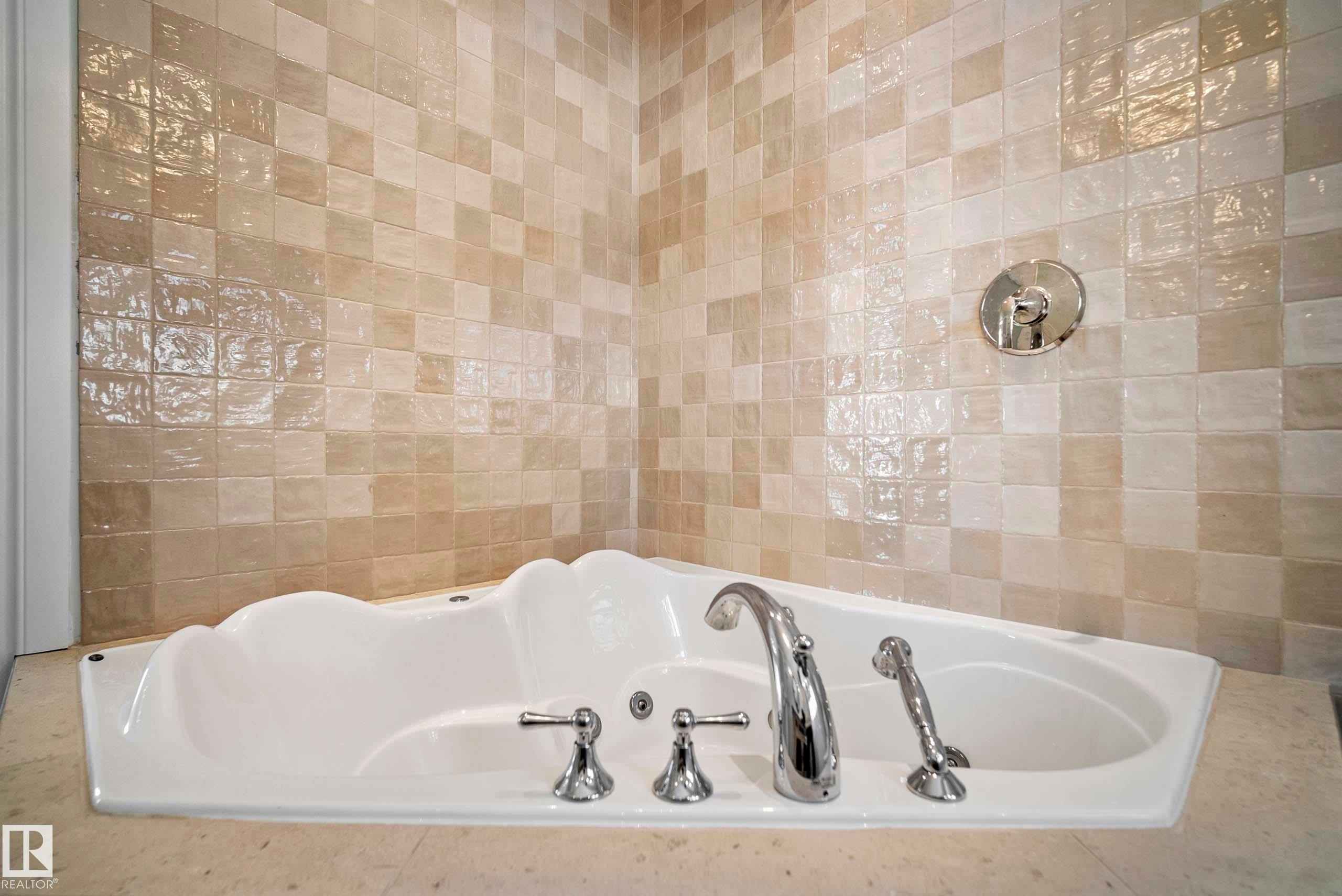 Built-in jetted tub with polished chrome fixtures, set against a tiled wall featuring varied square tiles - 104 Bayview Drive, Rural Parkland County, AB - Indoor Photo Showing Bathroom