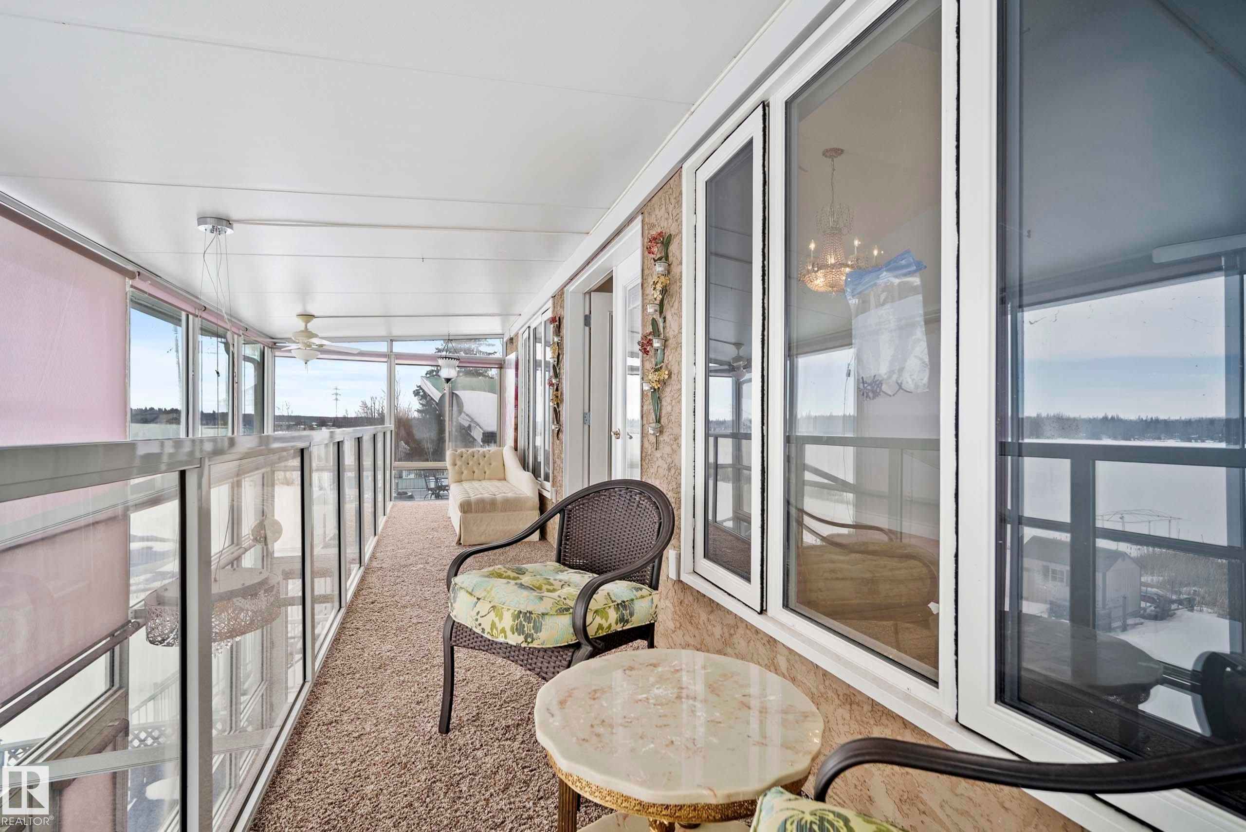 Enclosed sunroom featuring extensive glazing, textured wall finishes, and a neutral carpeted floor - 104 Bayview Drive, Rural Parkland County, AB - With Balcony With Exterior