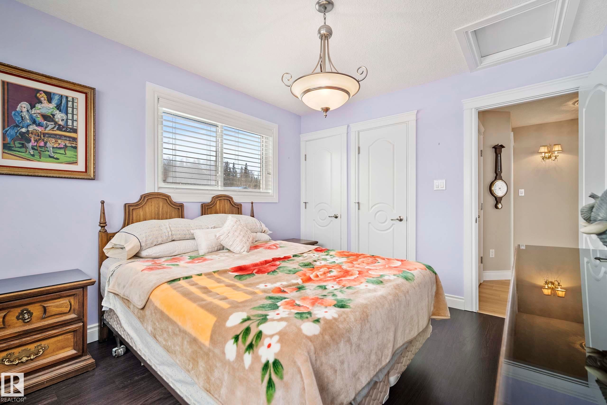 Bedroom featuring dark wood-finish flooring, two white panel doors, a large window with blinds, and a built-in ceiling light fixture - 104 Bayview Drive, Rural Parkland County, AB - Indoor Photo Showing Bedroom