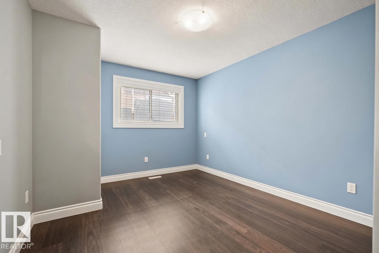 Spacious room featuring wood-finish flooring, light blue and grey wall paint, white baseboards, and a window with blinds - 104 Bayview Drive, Rural Parkland County, AB - Indoor Photo Showing Other Room