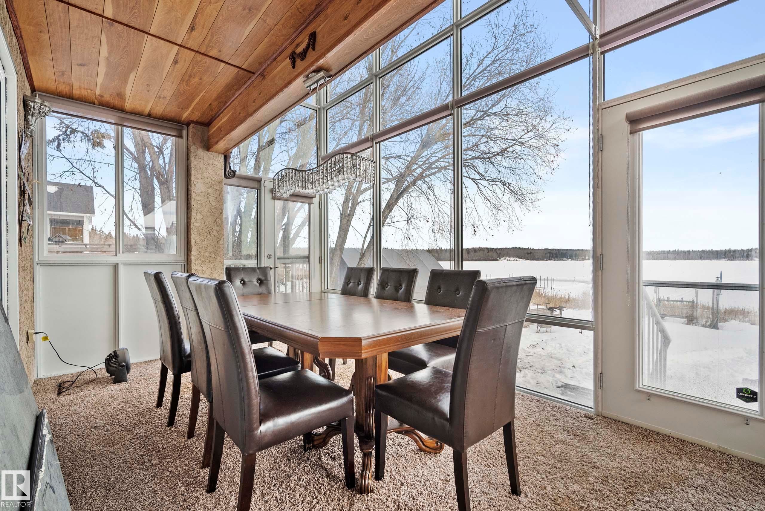 Sunroom with a full wall of floor-to-ceiling windows, wood-paneled ceiling, and a prominent chandelier - 104 Bayview Drive, Rural Parkland County, AB - Indoor Photo Showing Dining Room