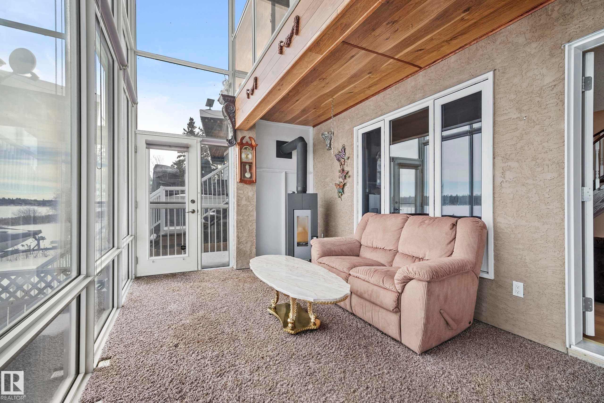 Enclosed sunroom featuring expansive fenestration, wood plank ceiling, and a modern freestanding fireplace - 104 Bayview Drive, Rural Parkland County, AB - Photo Showing Other Room