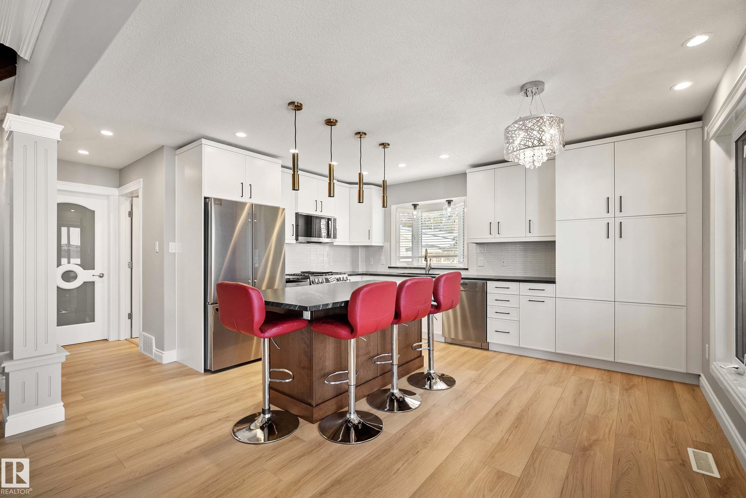 Contemporary kitchen featuring light wood-finish flooring, white cabinetry, stainless steel appliances, a center island with a dark countertop, and a decorative chandelier - 104 Bayview Drive, Rural Parkland County, AB - Indoor Photo Showing Kitchen With Upgraded Kitchen