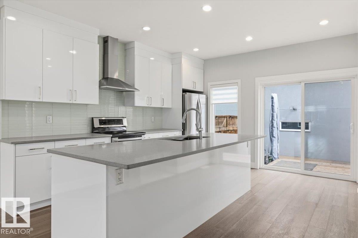 Modern kitchen featuring a large island with a sink, white cabinetry, stainless steel appliances, and wood-finish flooring - 9933 79 Street, Edmonton, AB - Indoor Photo Showing Kitchen With Stainless Steel Kitchen With Upgraded Kitchen