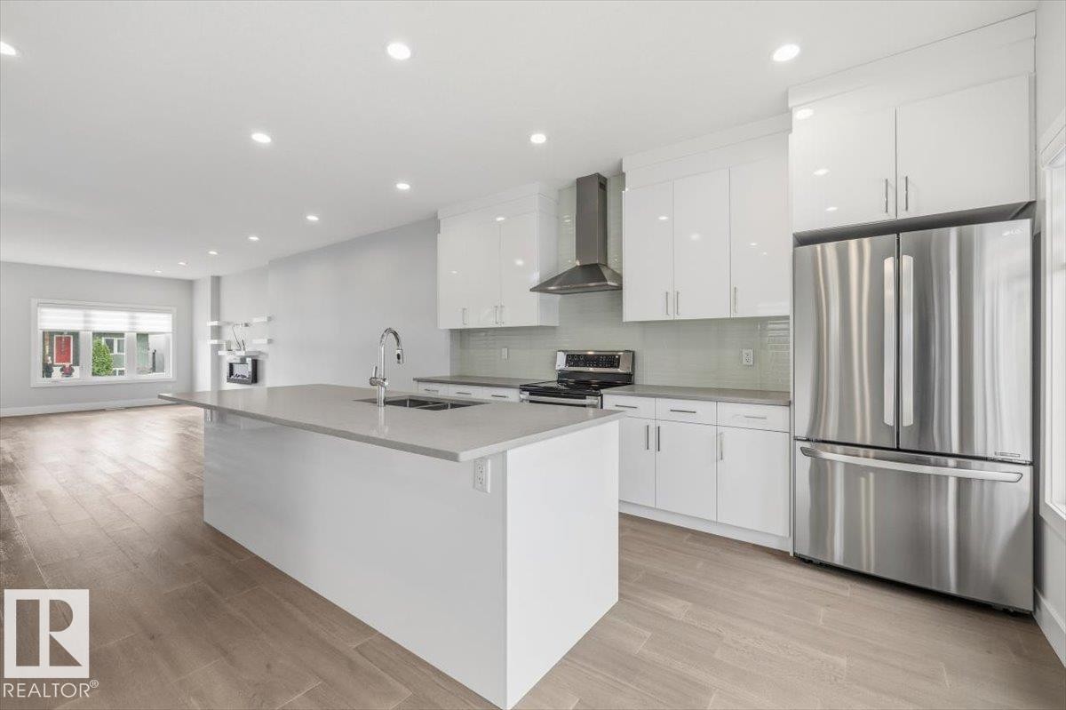 Modern kitchen featuring an expansive island with an undermount sink, white flat-panel cabinetry, stainless steel appliances, and wood-finish flooring - 9933 79 Street, Edmonton, AB - Indoor Photo Showing Kitchen With Stainless Steel Kitchen With Upgraded Kitchen