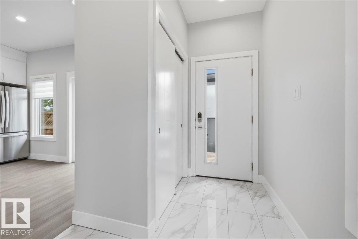 Entryway featuring large format white tile flooring, a solid panel front door with a vertical frosted glass insert, and a double-door closet - 9933 79 Street, Edmonton, AB - Indoor Photo Showing Other Room