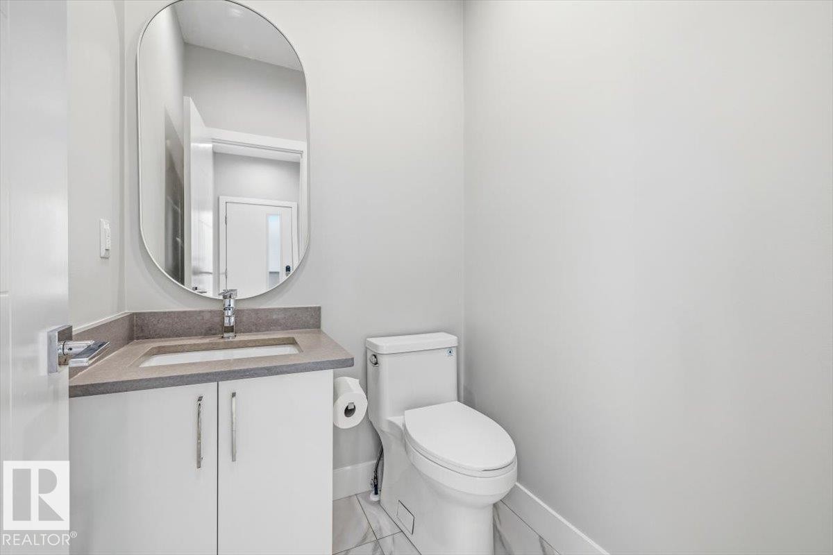 Powder room featuring a white vanity with integrated sink, stone-finish countertop, and a contemporary oval mirror - 9933 79 Street, Edmonton, AB - Indoor Photo Showing Bathroom