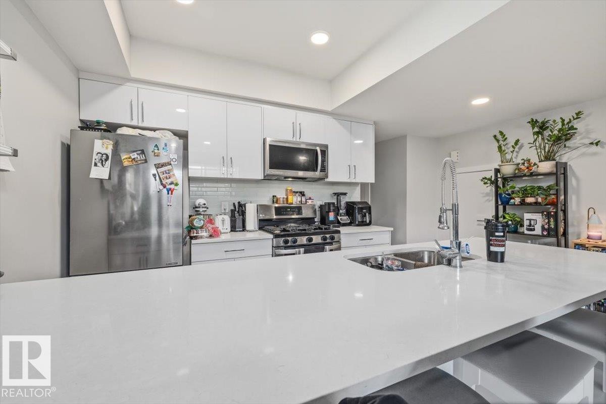 Modern kitchen featuring a large island with an undermount sink, stainless steel appliances, white flat-panel cabinetry, and a subway tile backsplash - 9933 79 Street, Edmonton, AB - Indoor Photo Showing Kitchen With Stainless Steel Kitchen With Double Sink
