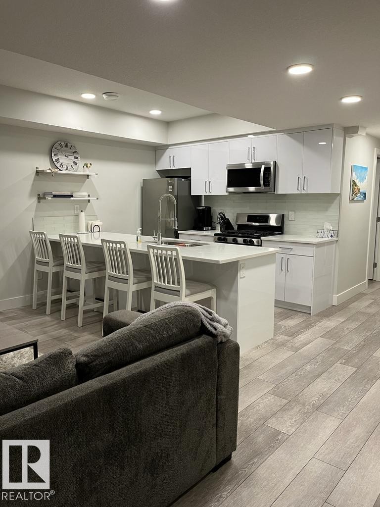 Modern kitchen featuring white cabinetry, stainless steel appliances, a white tile backsplash, and a large island with seating - 9933 79 Street, Edmonton, AB - Indoor Photo Showing Kitchen With Stainless Steel Kitchen